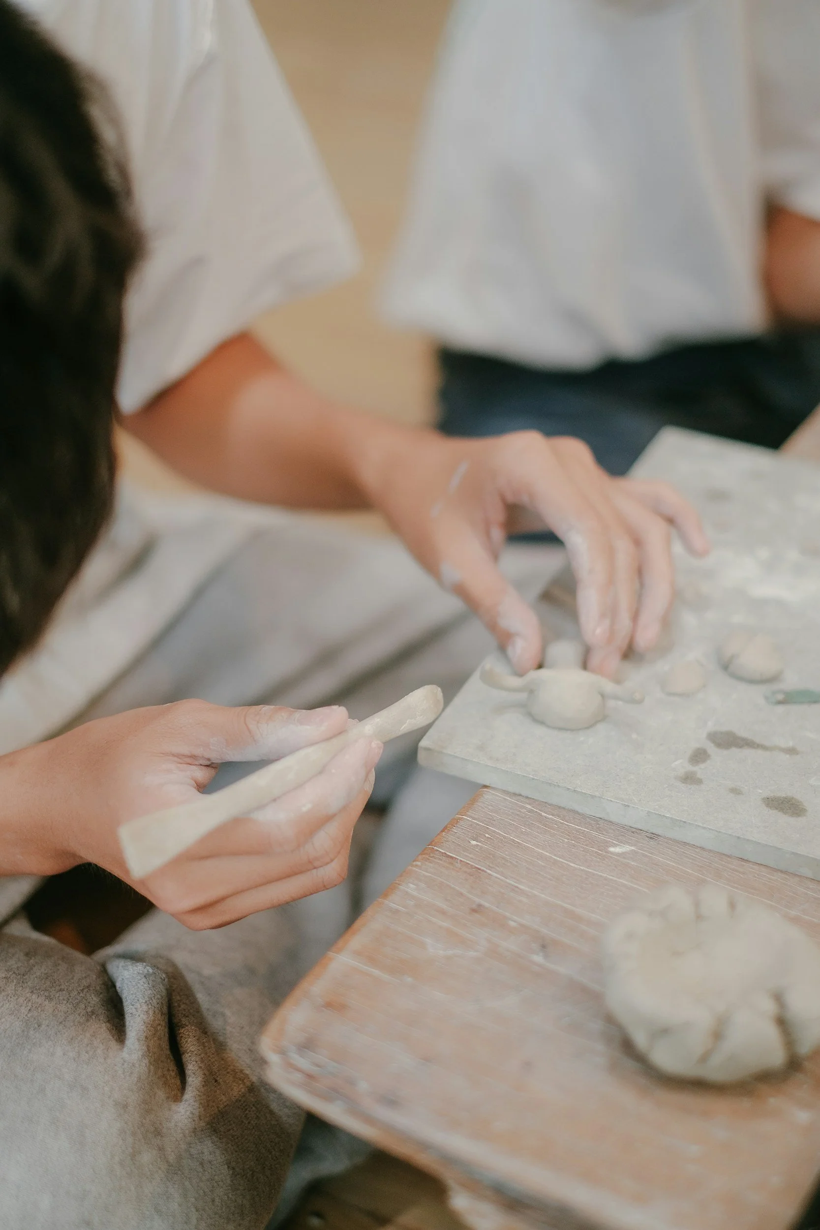 Two people shape clay into small balls and a rod in a pottery workshop.