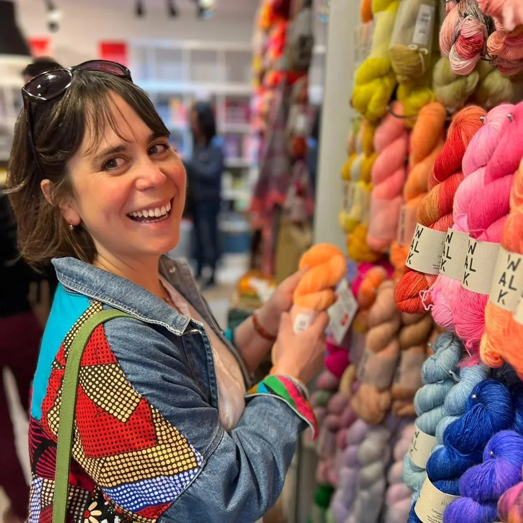Woman shopping for colorful yarn in a craft store, smiling and holding some orange yarn.