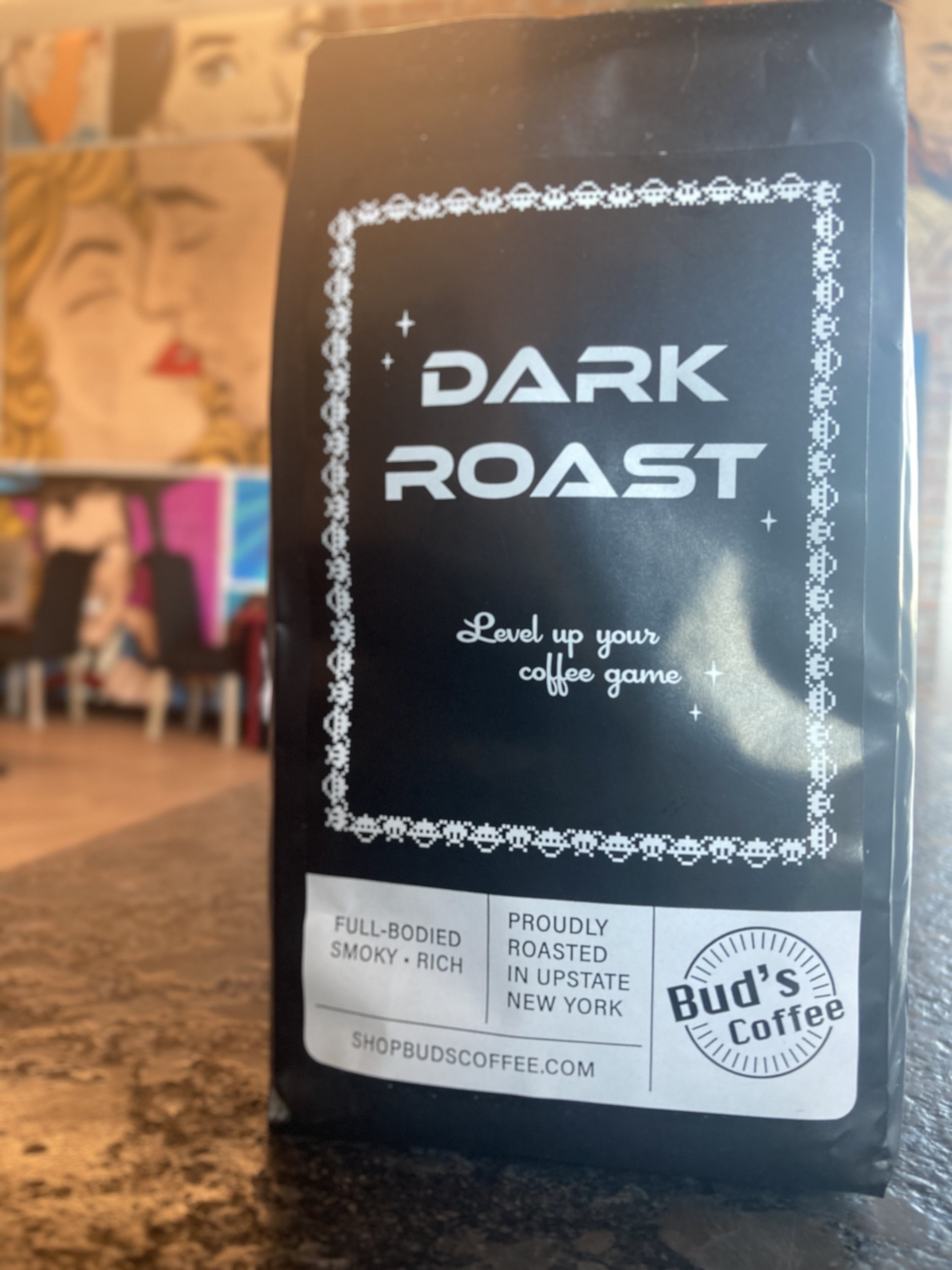 Bud's Dark Roast Coffee bag featured in front of our arcade tables and iconic pop art wallpaper in out Bud's on the Hudson coffeehouse located at 10 Starbuck Dr, Green Island, New York.