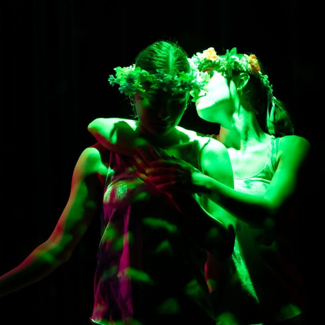 two women embrace with flower crowns and green light