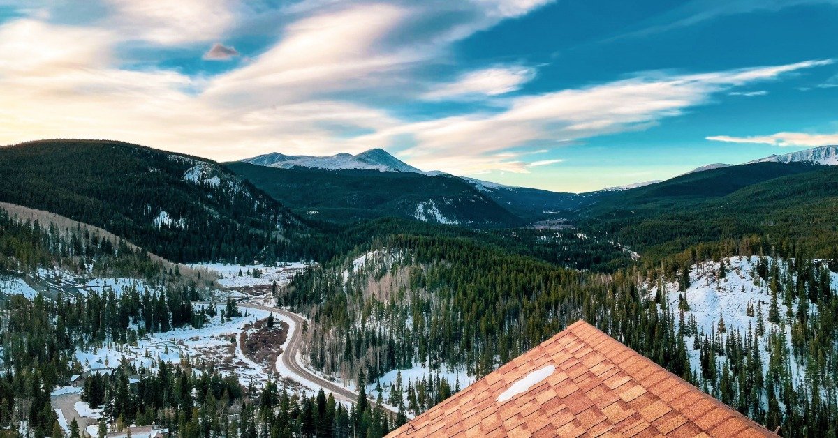 A view from a house's rooftop of snow-capped mountains in Breckenridge, Colorado. Many trees are visible.