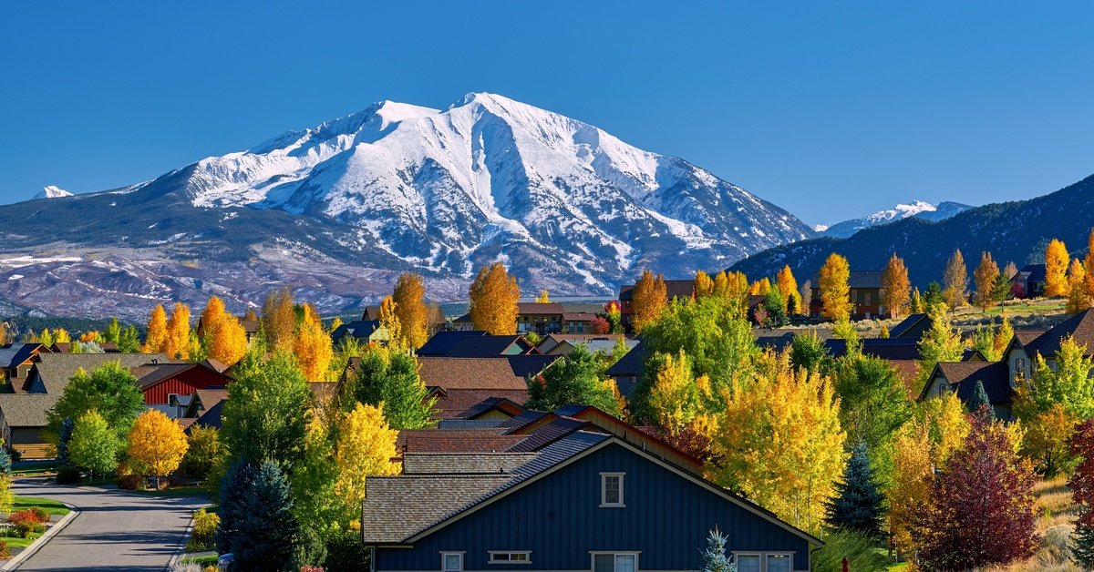 A residential neighborhood features winding roads, houses, and autumn trees. It sits near distant mountains.