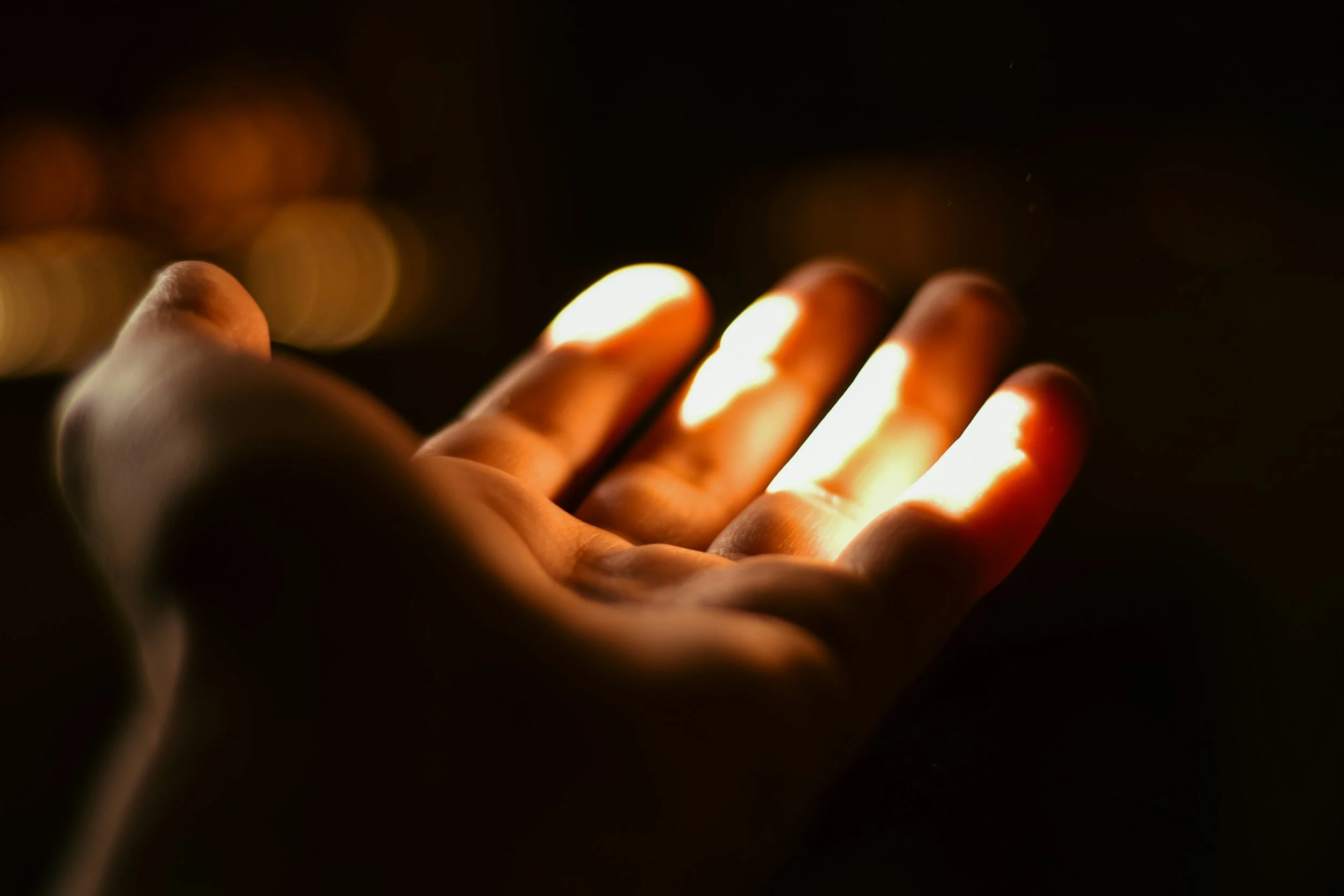 A hand in darkness with fingers illuminated by glowing light, creating a warm glow on the fingers.