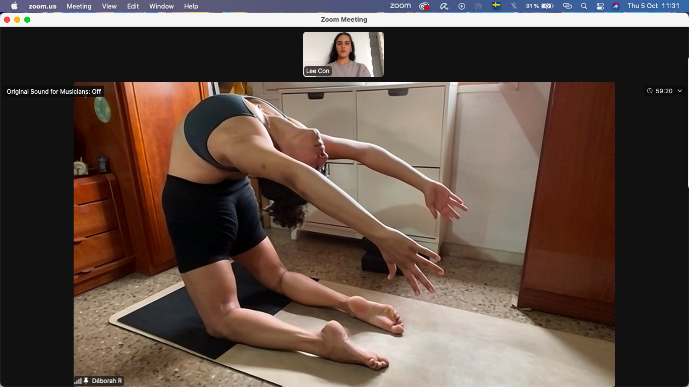 Woman practicing yoga on a mat in her home with a private yoga teacher guiding her into Kapotasana.