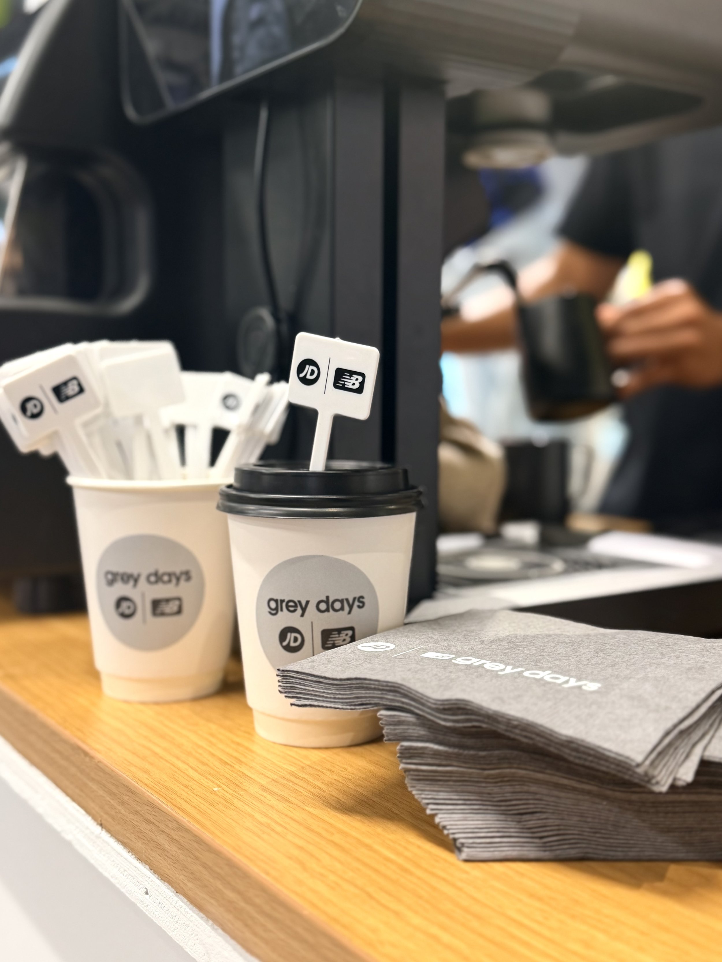 Custom-branded coffee cups and drink toppers at the JD Sports x New Balance Grey Days activation, featuring specialty coffee catering by Villette at Dolphin Mall in Miami.