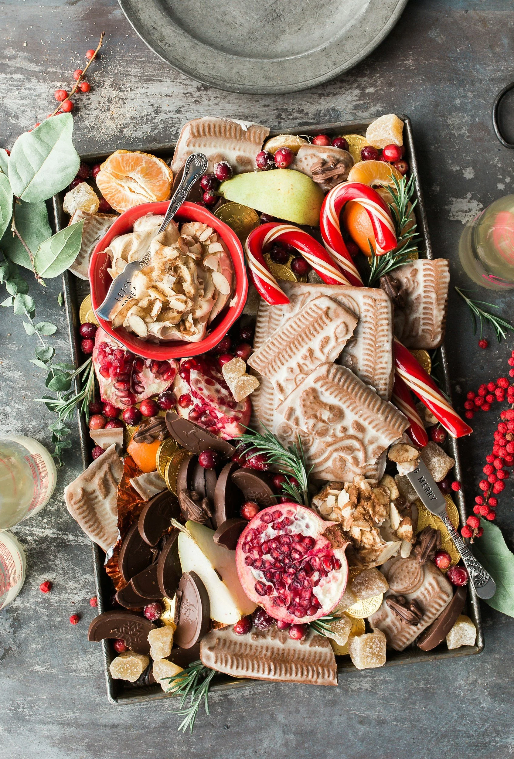 A Christmas tray with assorted chocolates, candies, fruit, and holiday decorations, including candy canes and sprigs of holly.