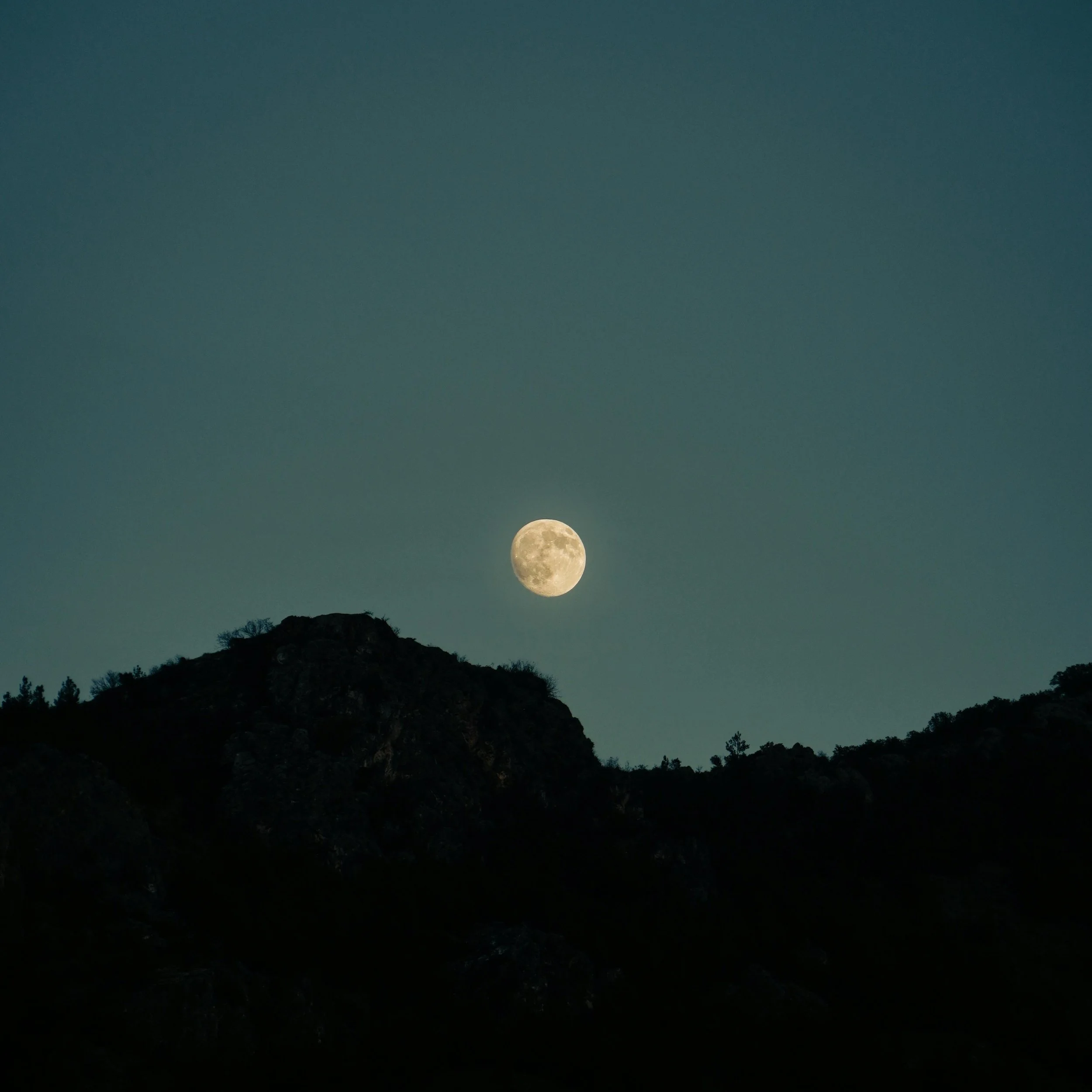 Full moon rising over a silhouette of a mountain range at night.
