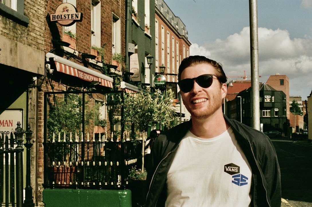 A smiling, red bearded man stands in front of The Ginger Man Bar on a sunny day in Dublin, Ireland.