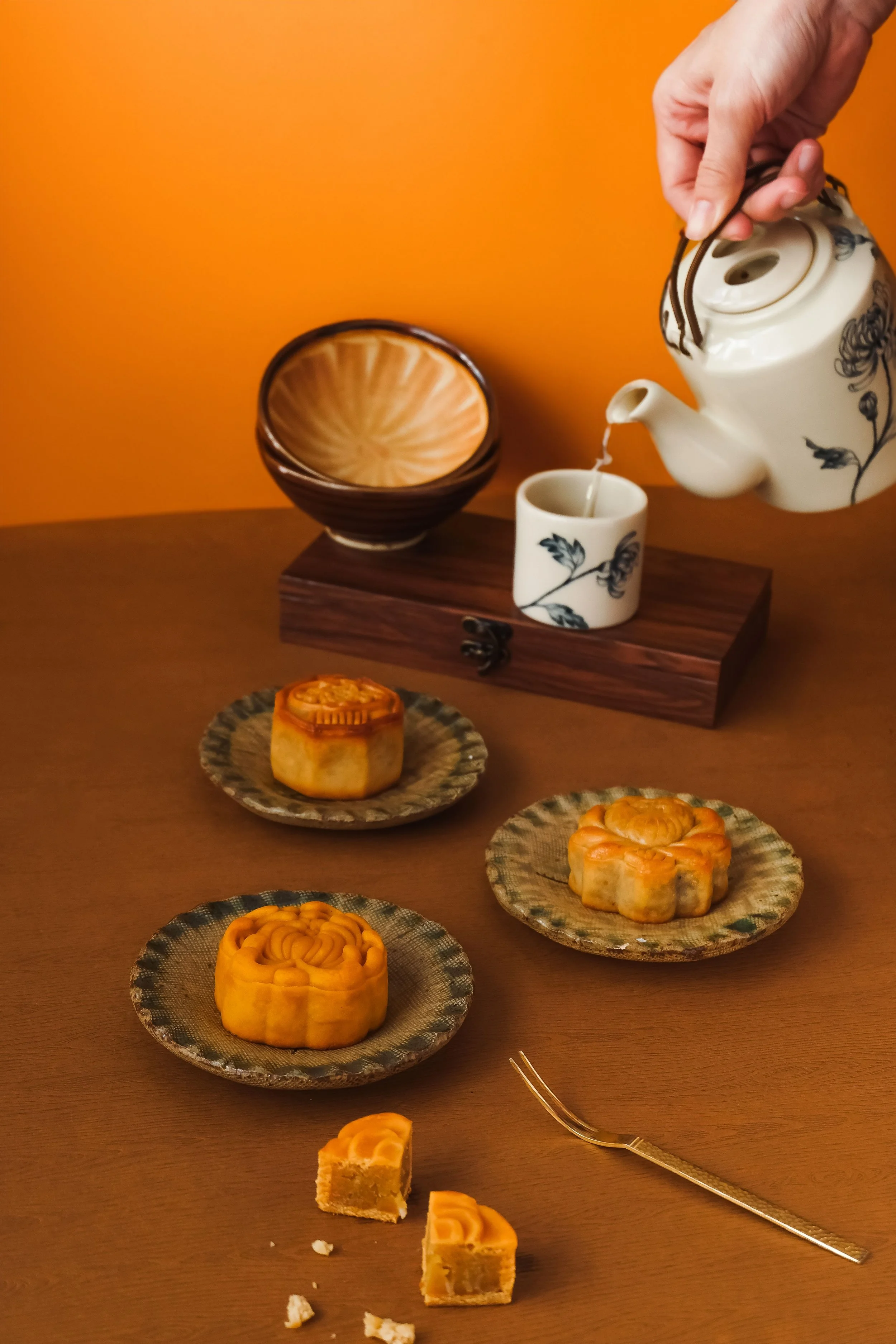 Three small Vietnamese mooncakes on a brown table with wooden plating and ceramic cutlery