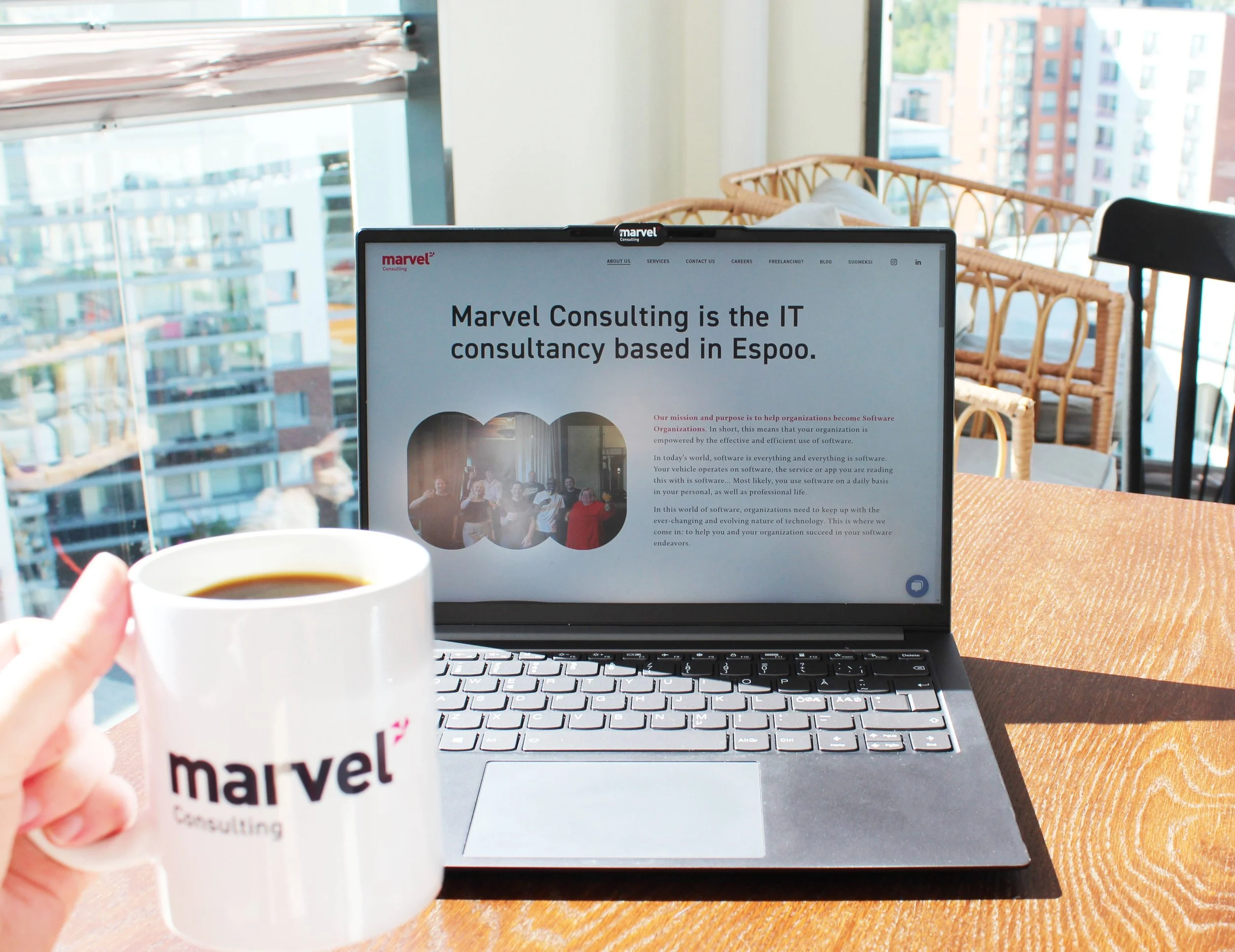Picture of a computer with the text "Marvel Consulting is the IT consultancy in Espoo", and on the left side there is a hand holding a coffee mug.