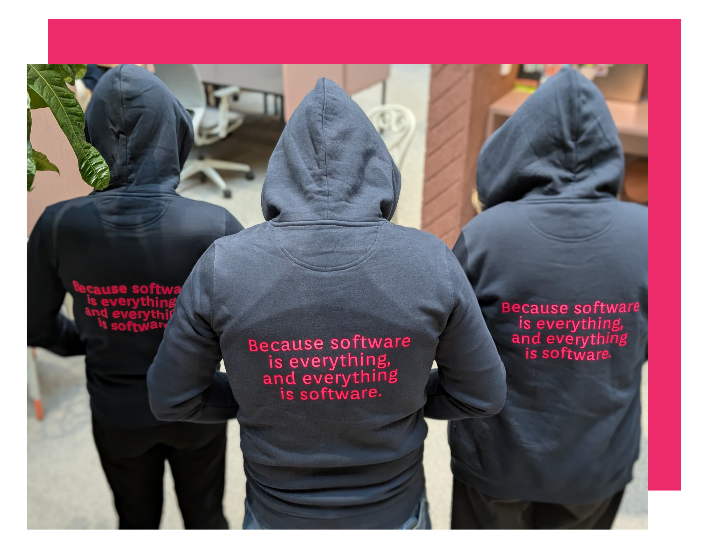 kolme ihmistä kuvattuna rivissä takaapäin, päällään hupparit joissa lukee "Because software is everything and everything is software"