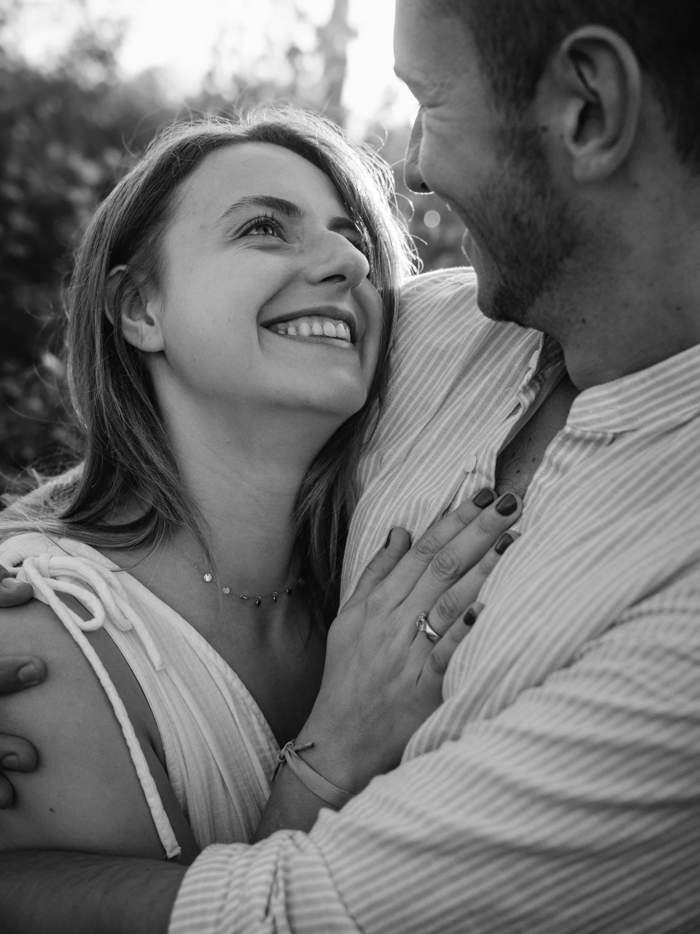 Un couple souriant s'étreint tendrement dans un cadre extérieur, en noir et blanc.