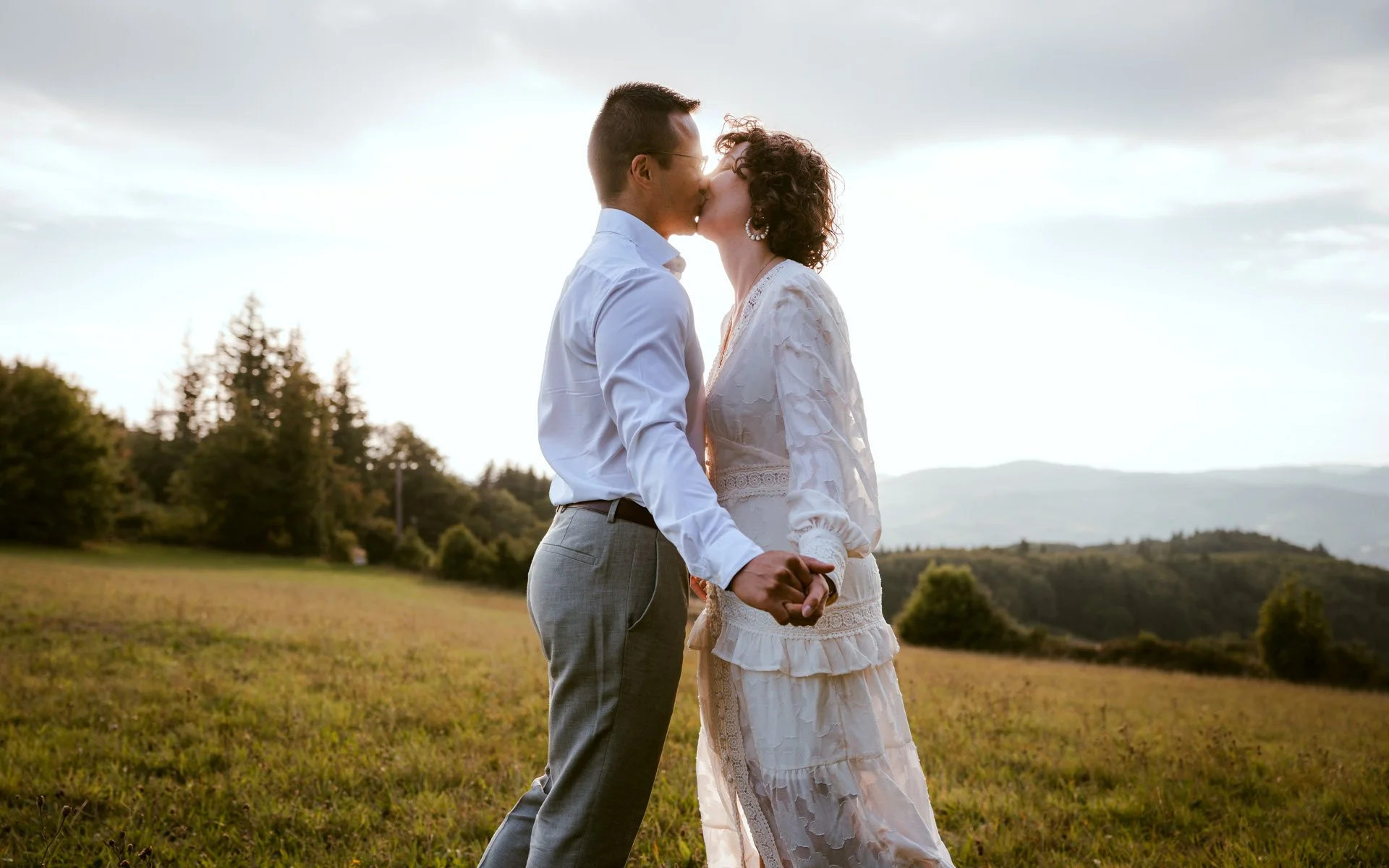 Un couple s'embrasse dans un champ lors d'un coucher de soleil, avec des montagnes en arrière-plan.