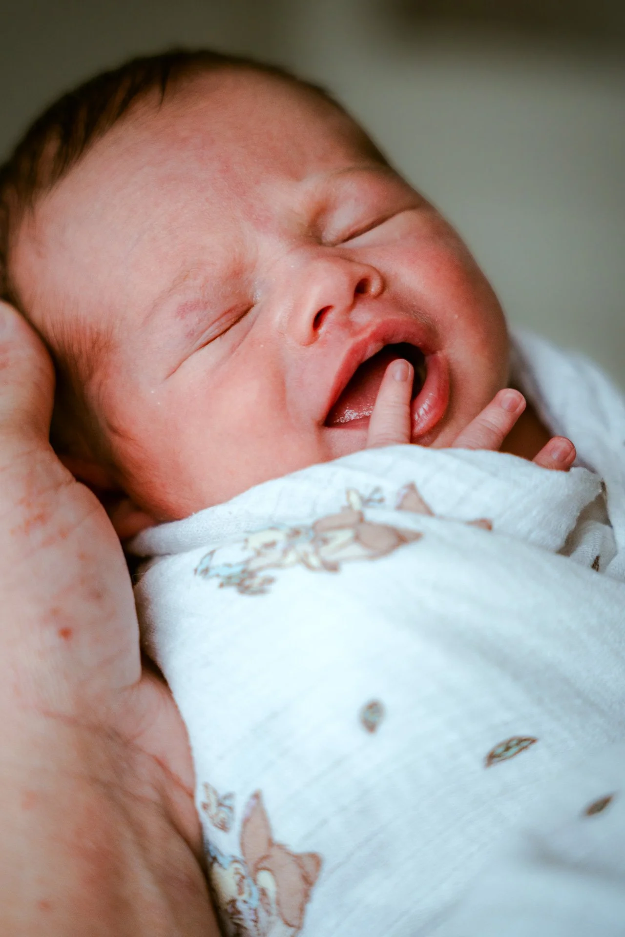 Un bébé endormi avec un doigt dans la bouche, enroulé dans une couverture blanche avec un motif floral.