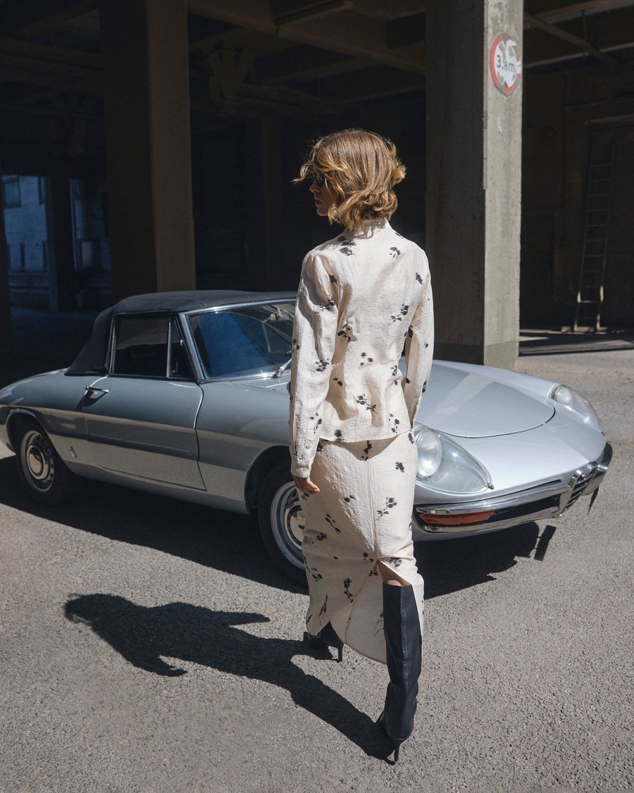 Vrouw met zonnebril wandelt naar vintage wagen. Ze draagt een halflange rok MSCHRianne Skirt AOP met bloemenprint van Moss Copenhagen.