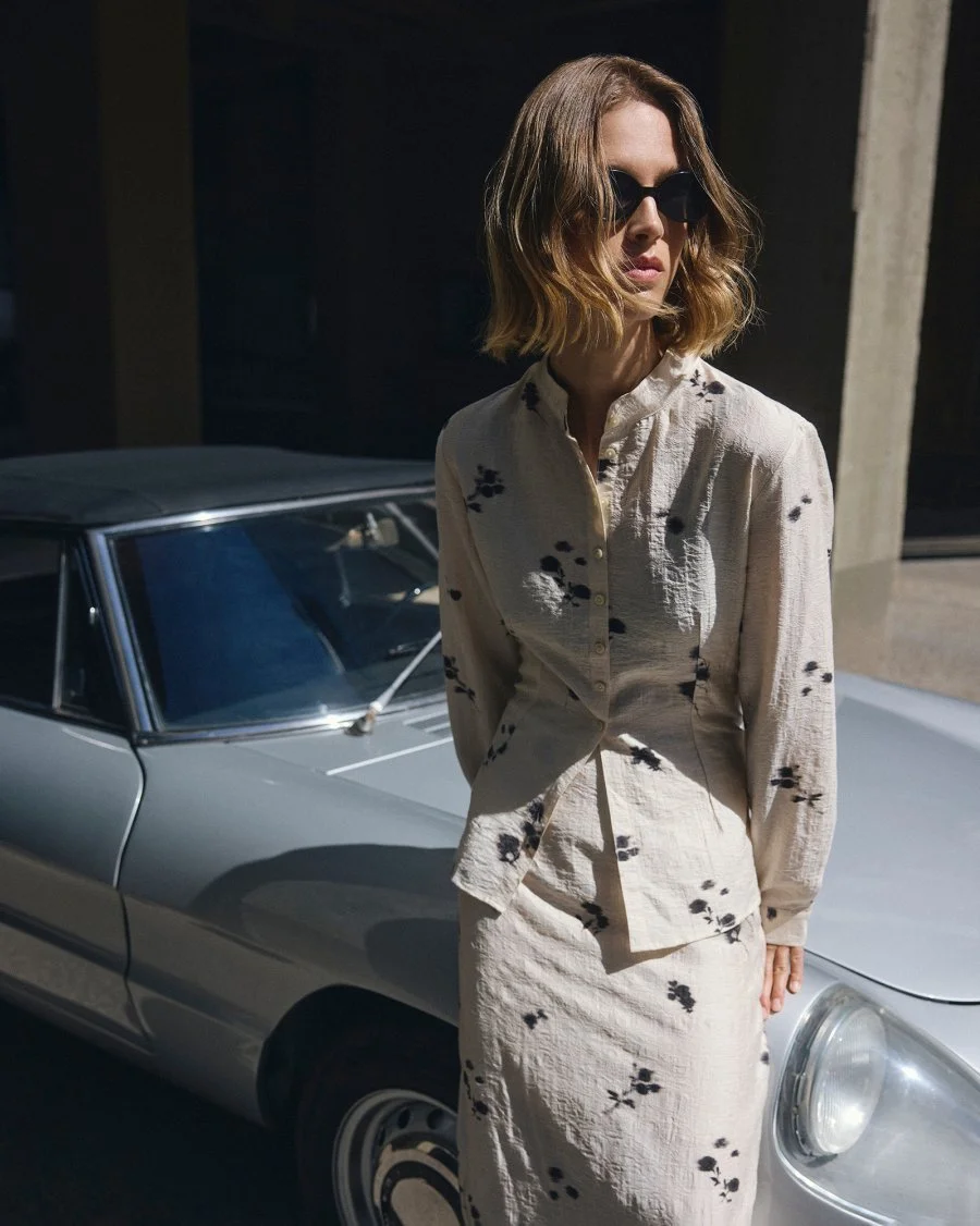 Vrouw met zonnebril leunt tegen vintage wagen. Ze draagt een halflange rok MSCHRianne Skirt AOP met bloemenprint van Moss Copenhagen.