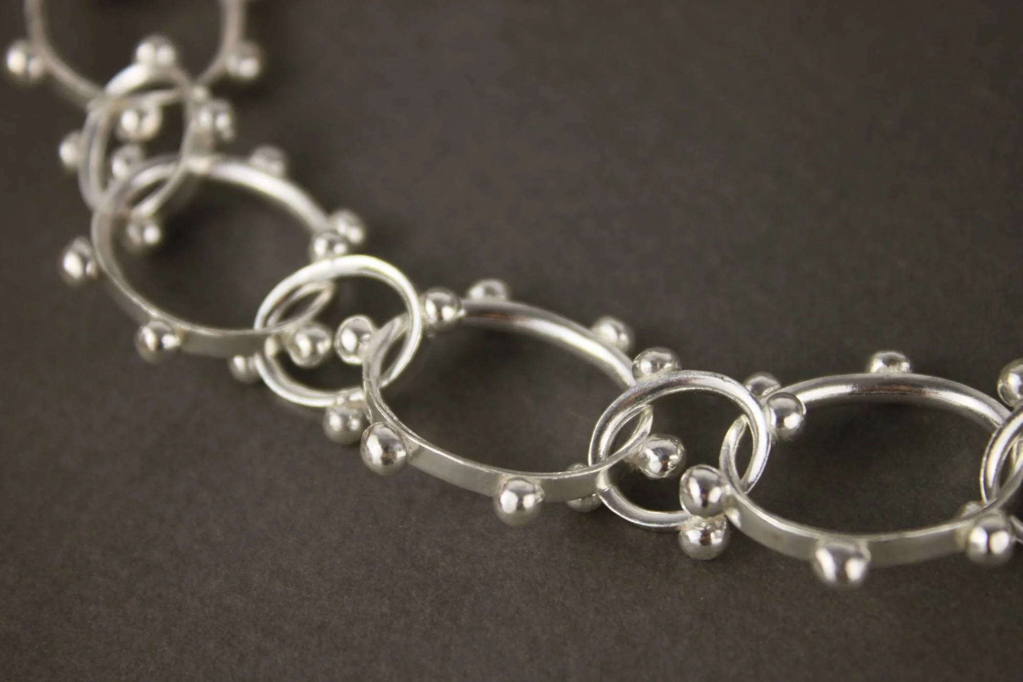 Close up of studded silver links of a chunky punk chain necklace on a grey background