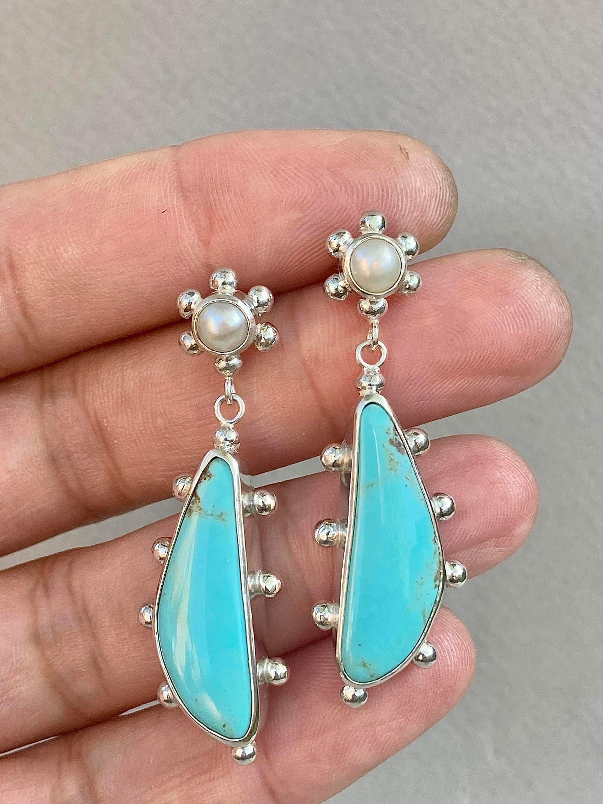 Long dangle earrings with stud backs with small round pearl cabochons and irregular shaped sky blue turquoise cabochons set in sterling silver bezels and decorated with silver studs