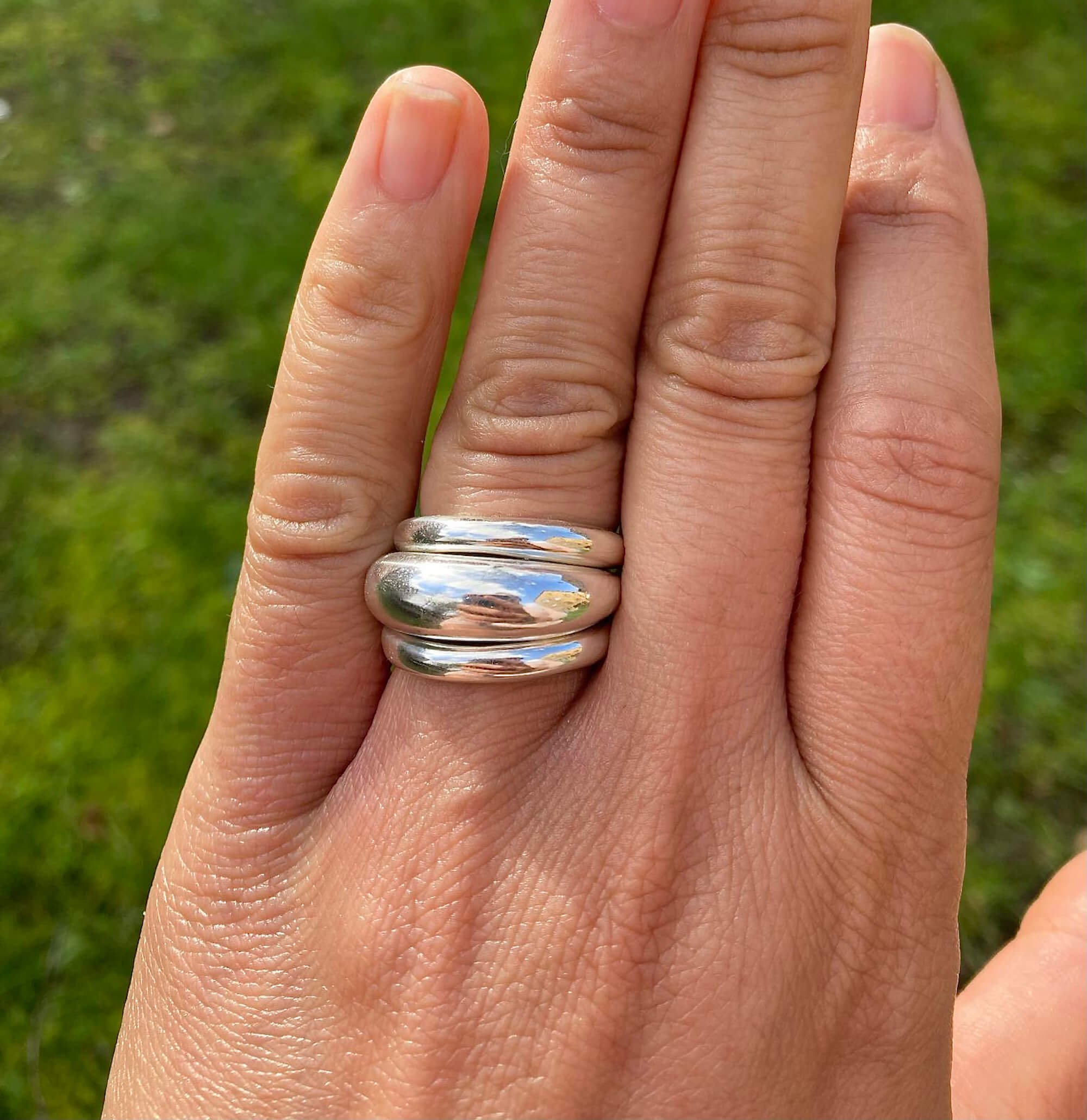 3 silver stacked bombe rings worn on a hand with a lawn in the background