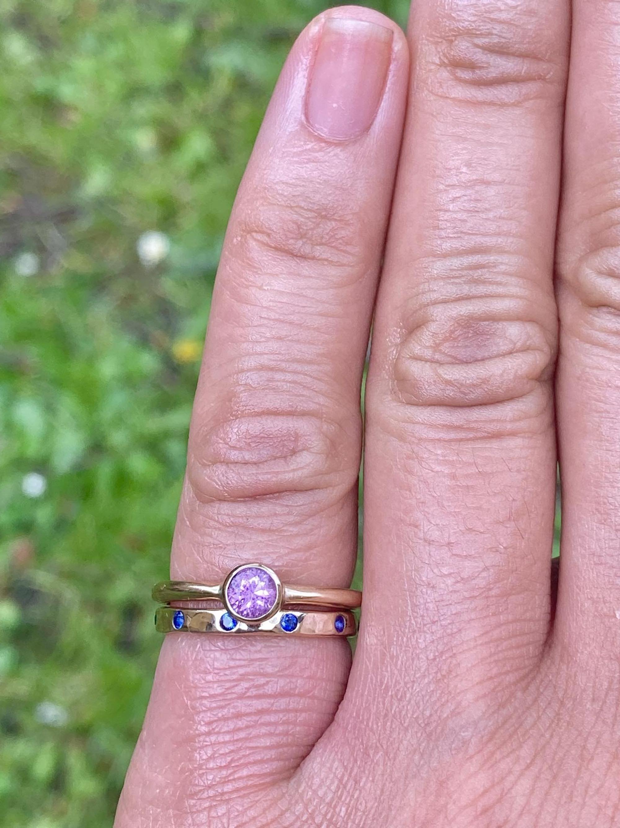 Hammered yellow gold eternity ring with blue sapphires next to pink sapphire gold ring