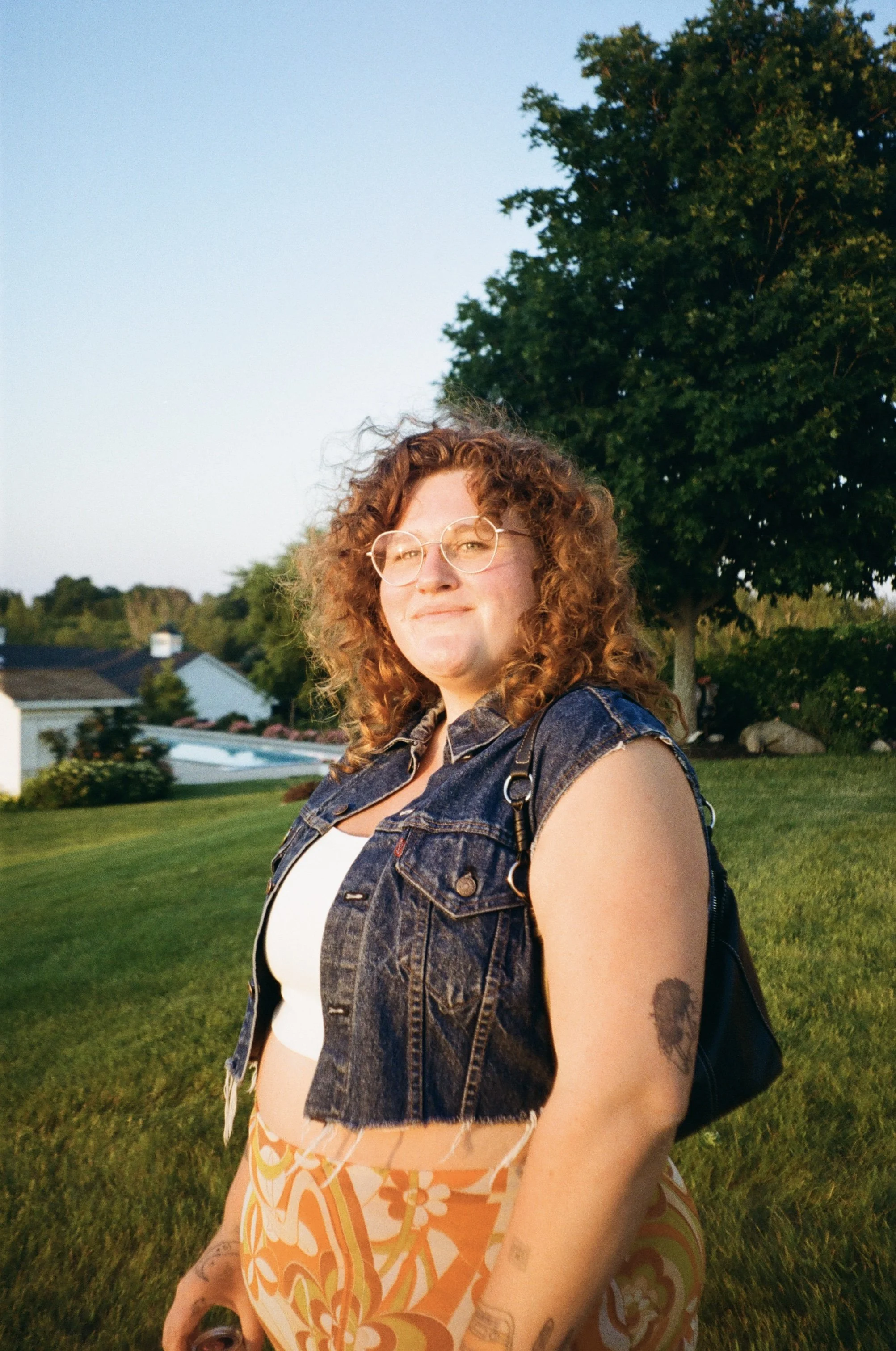 thirty year old woman with cut off jean jacket and skirt on standing in backyard at wedding afterparty