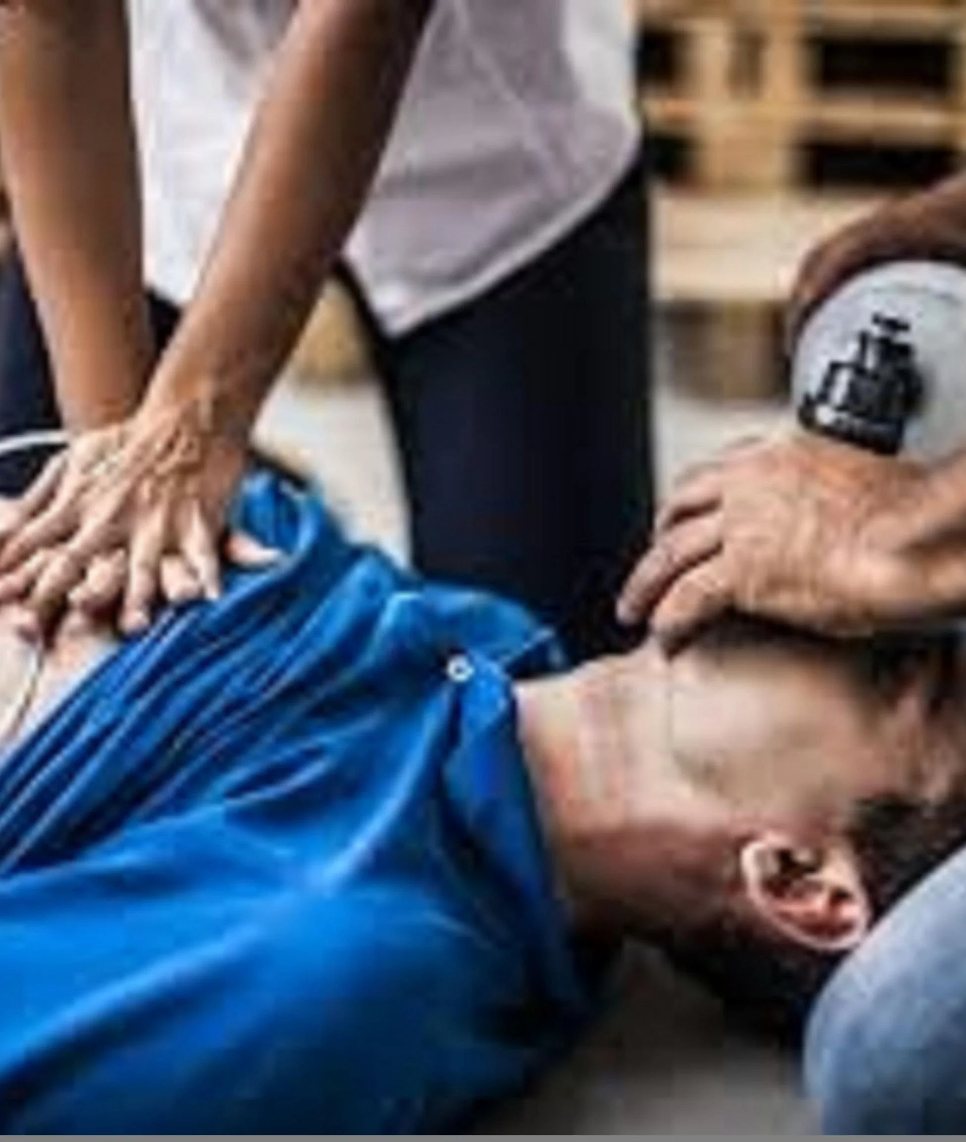 Group of five people practicing CPR on a training mannequin in a classroom.