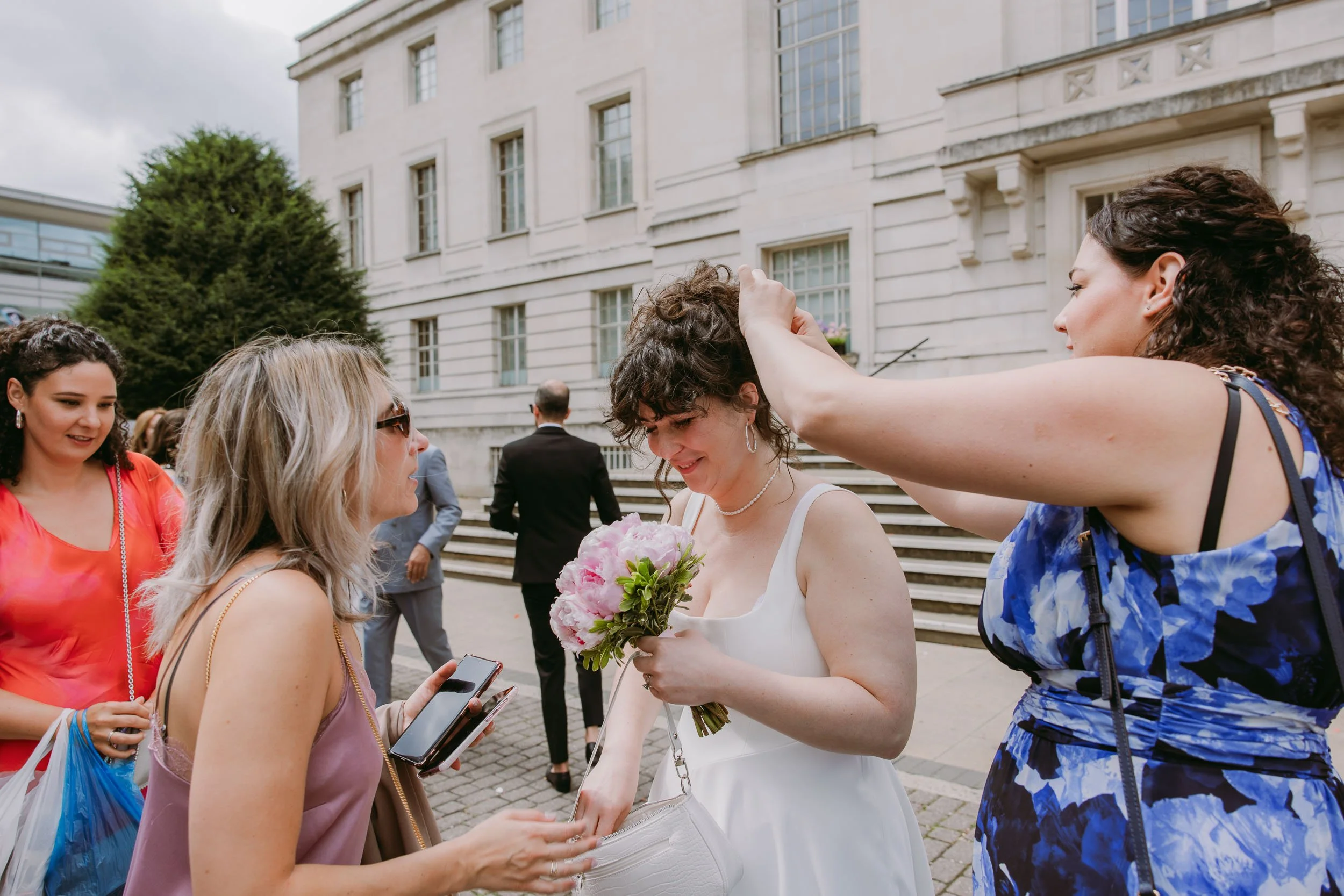 friends removing confetti from brides hair outside hackney town hall