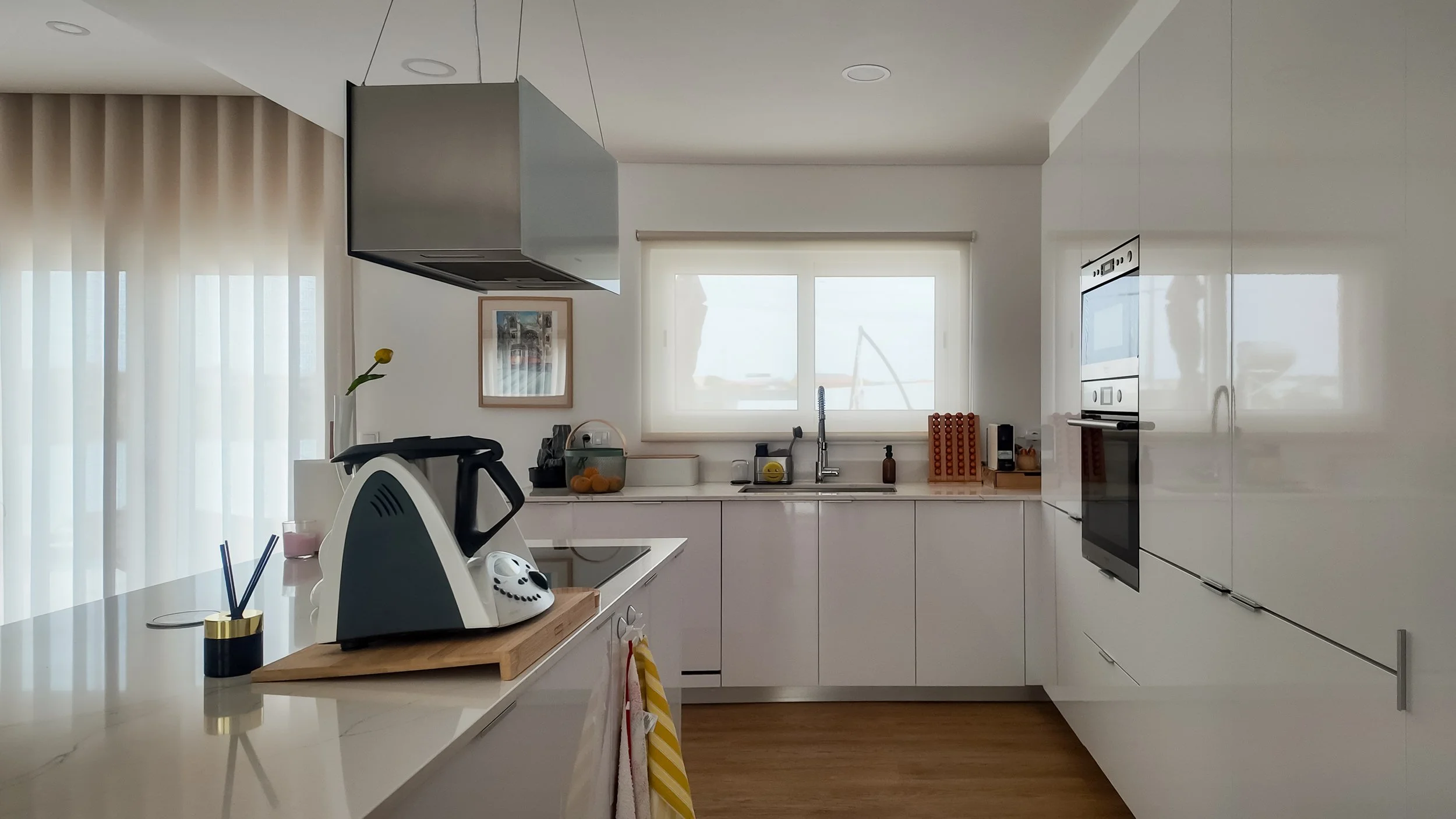 Cozinha moderna com armários brancos, bancada de mármore, parede de janelas grandes, eletrodomésticos embutidos, utensílios de cozinha e decoração minimalista.