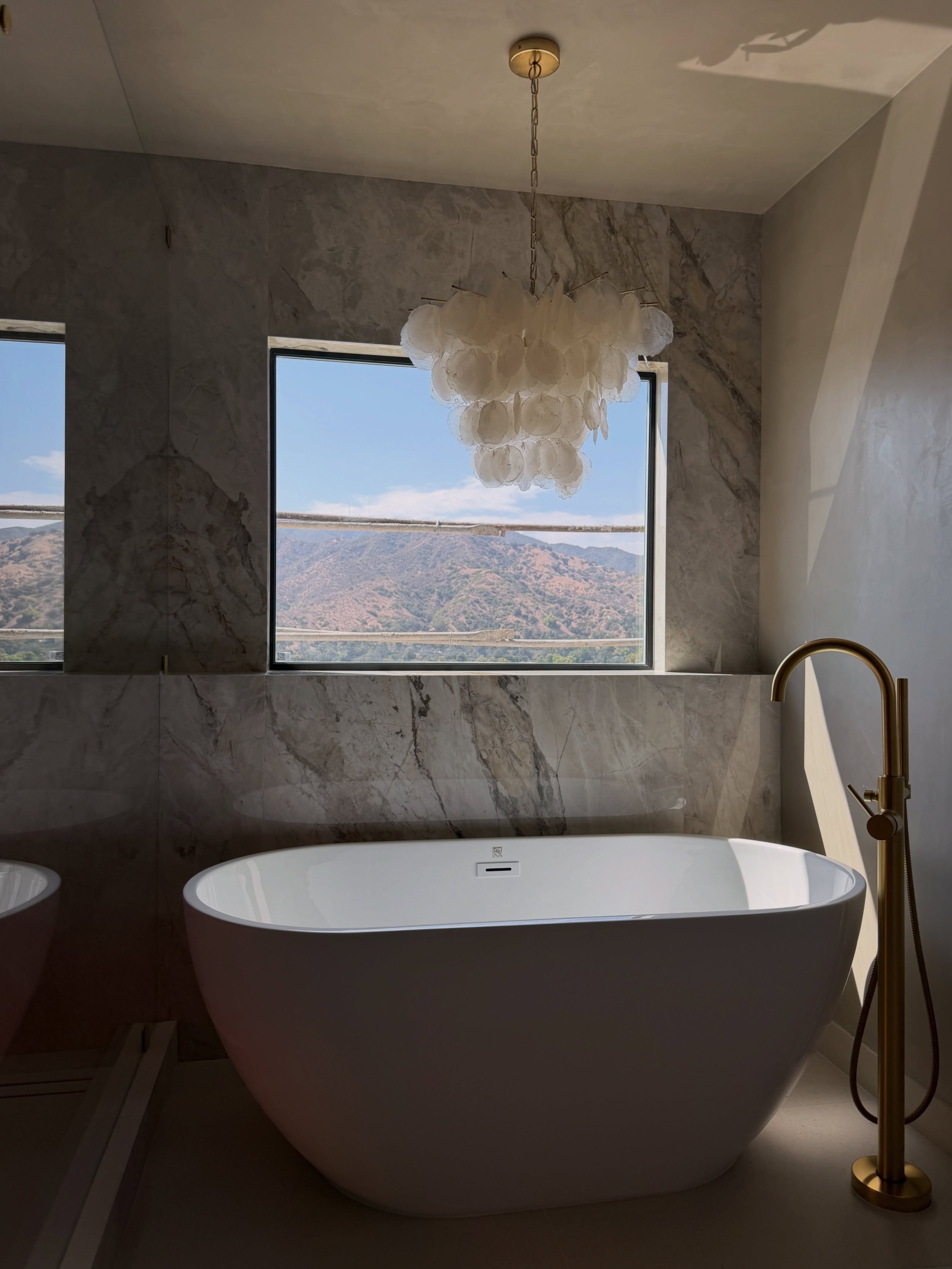 One of the most calming spaces in this full house remodel.
For the primary bathroom, I wanted the materials to do the work. Stone carried from the vanity wall into the shower and around the tub, while warm wood cabinetry, brass plumbing, arched mirro