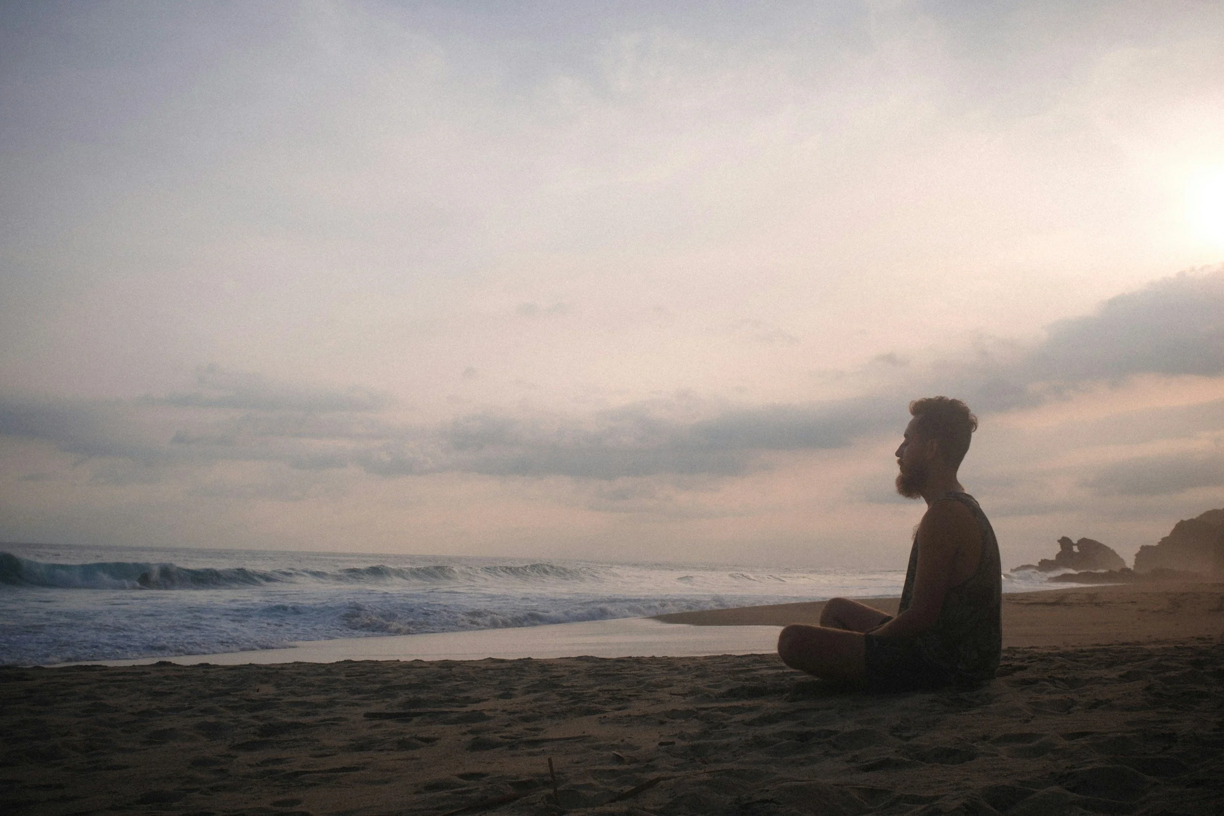 Man meditating and deep breathing on the beach at sunrise.