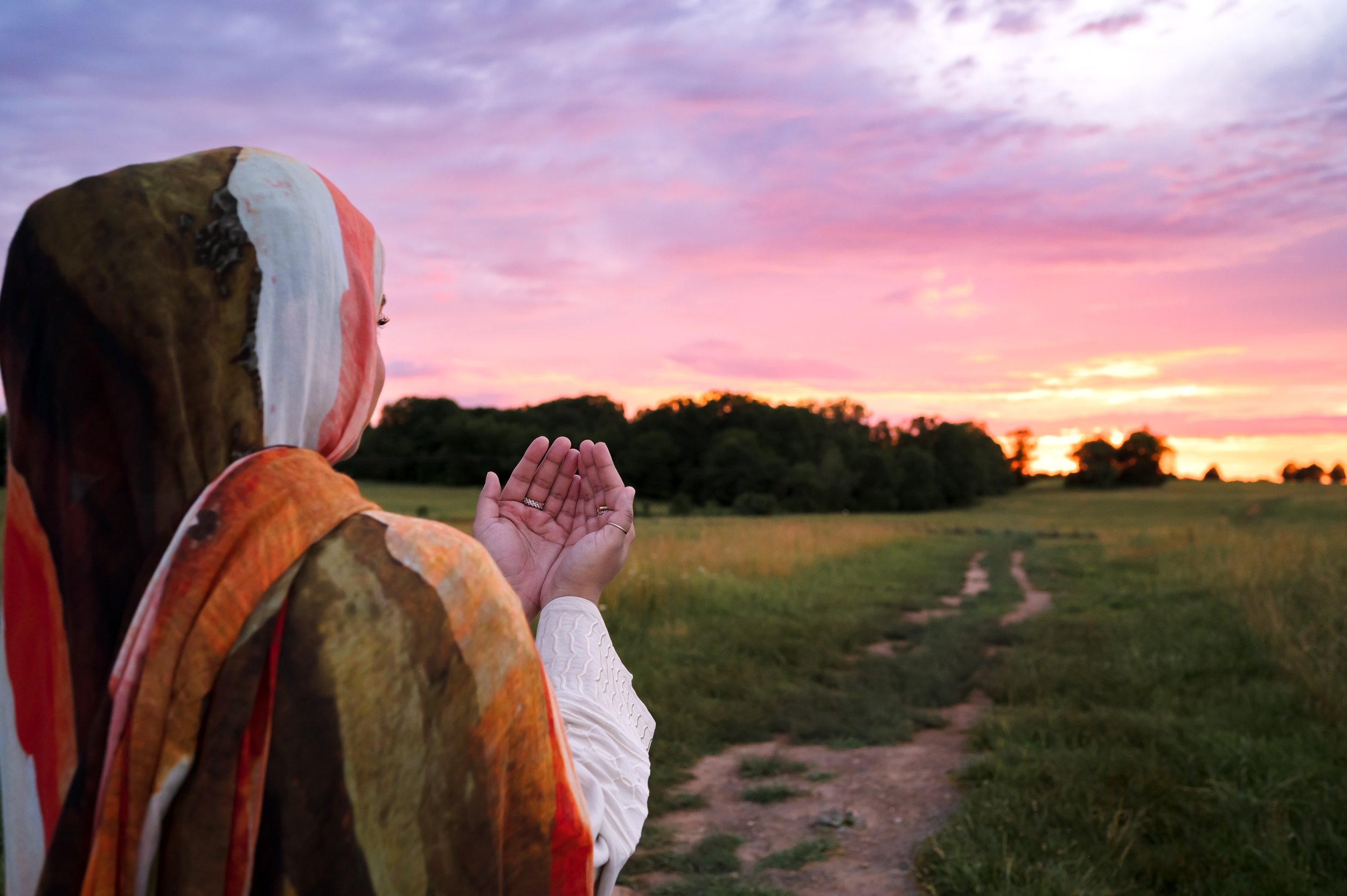 Hijabi making dua outside with the sunset in the background