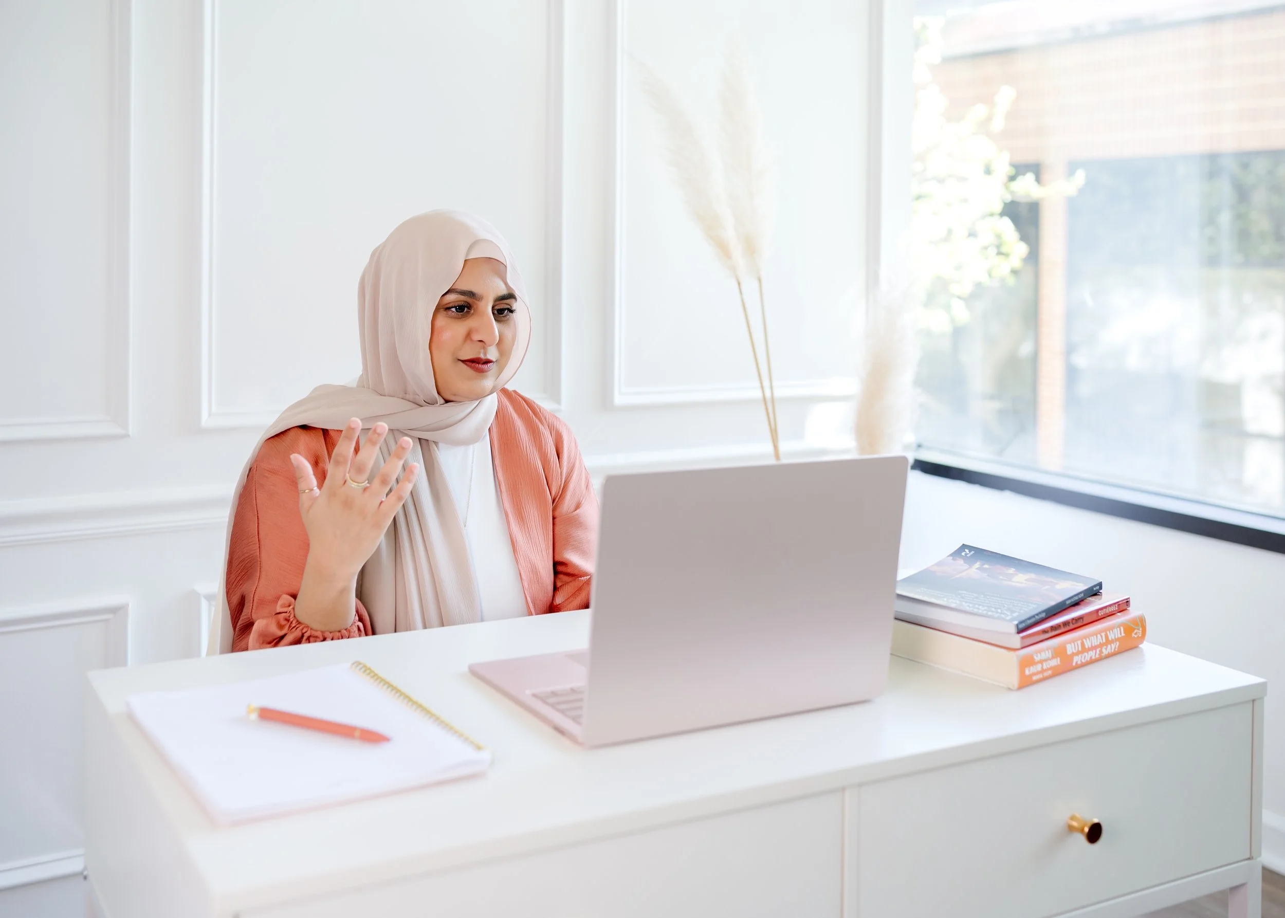 Natasha Deen wearing hijab conducting a virtual session from her laptop at a desk speaking with hand gestures
