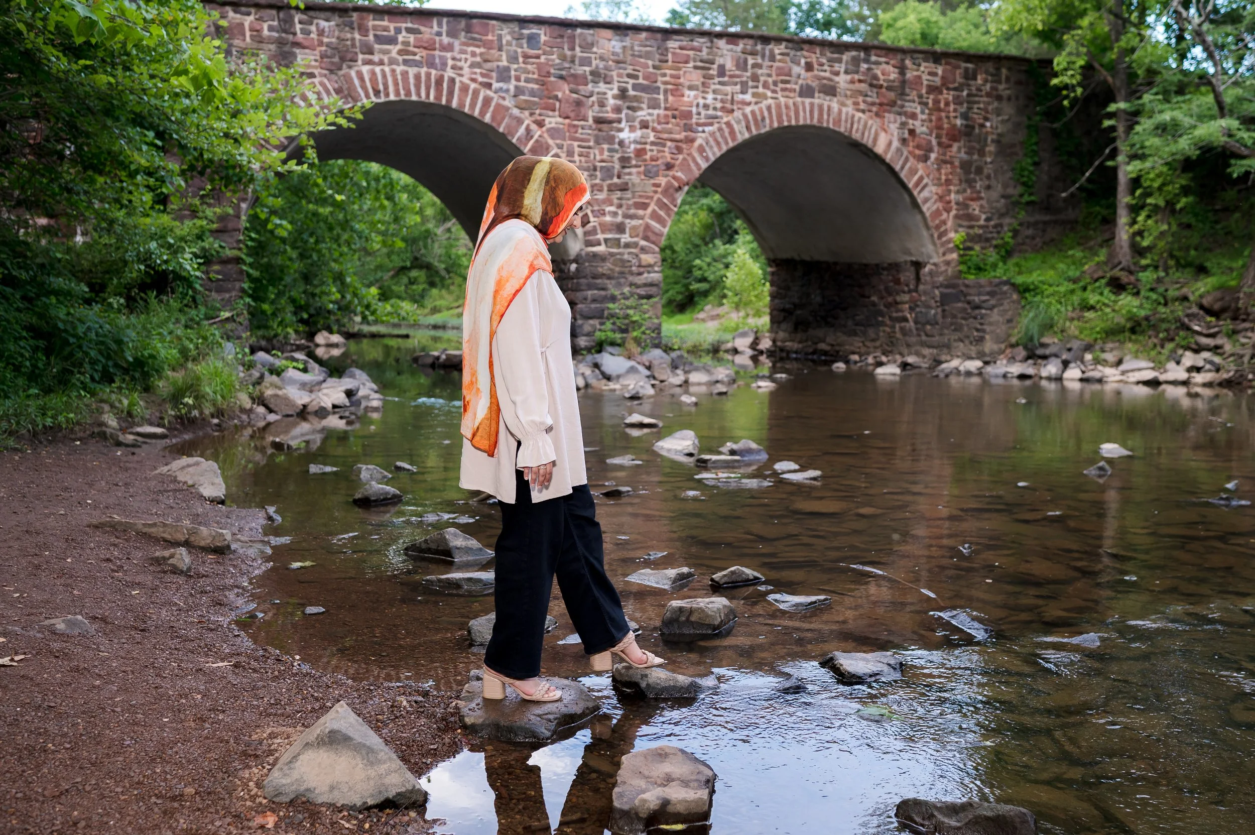 Hijabi looking down as she crosses a creek via step stones