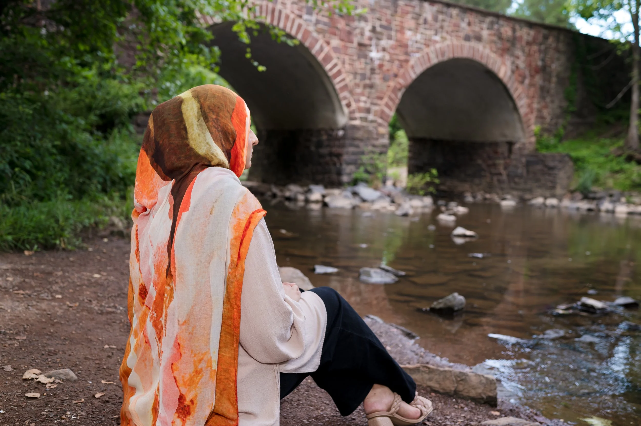 Hijabi sitting at a creek bank engaged in self-reflection.