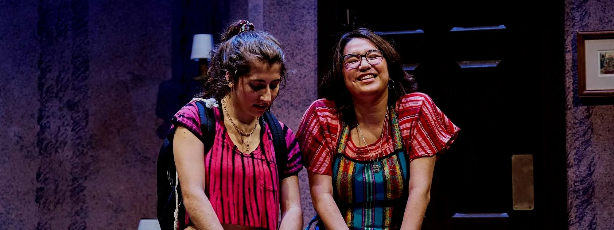 Two smiling women standing at a table with mixing bowls in a kitchen setting.