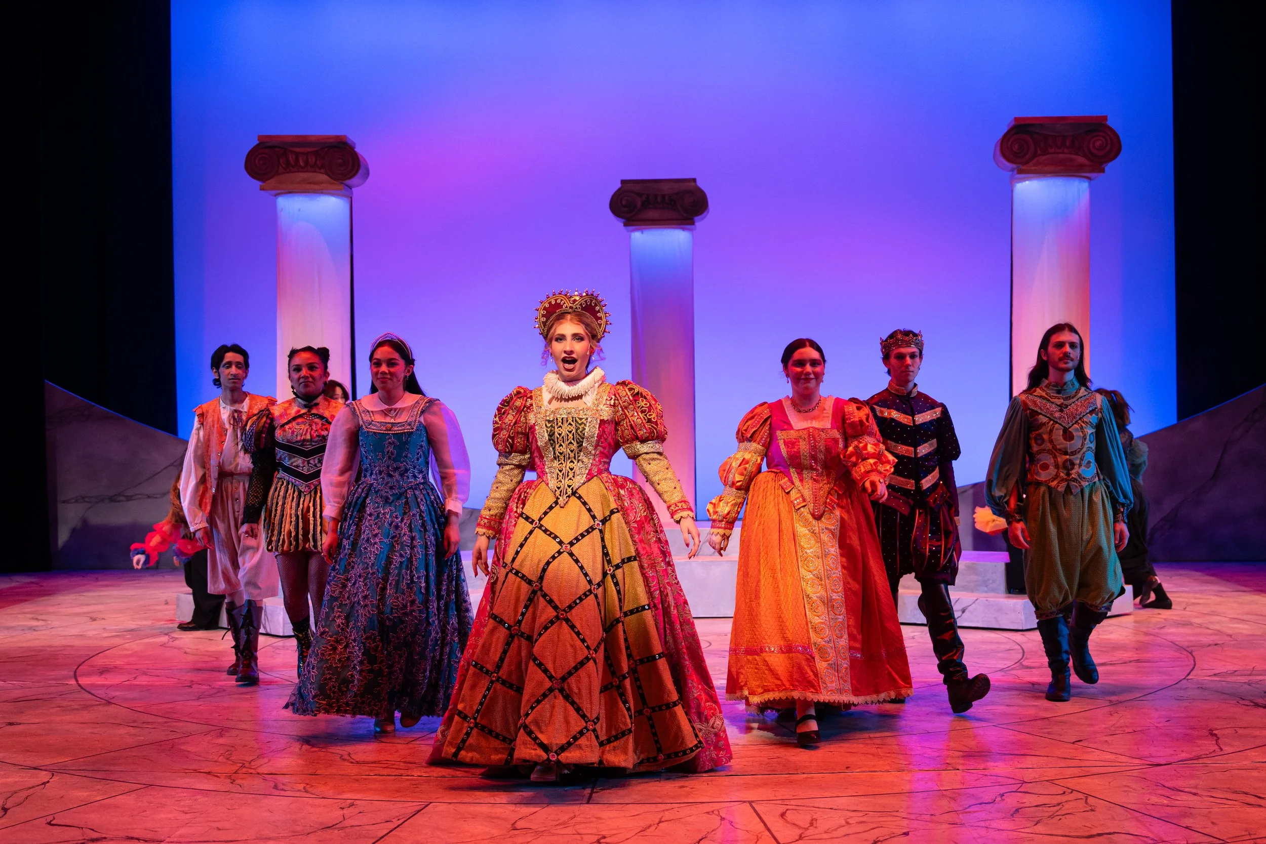 SCU "Head Over Heels" performance captures 7 actors on a stage in period  costume, with a woman in a large gown standing front and center. 