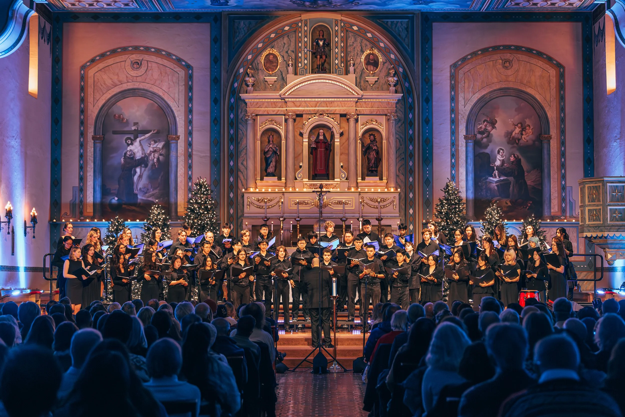 Choir all dressed in black sing in front of the Mission church with an audience watching on. 