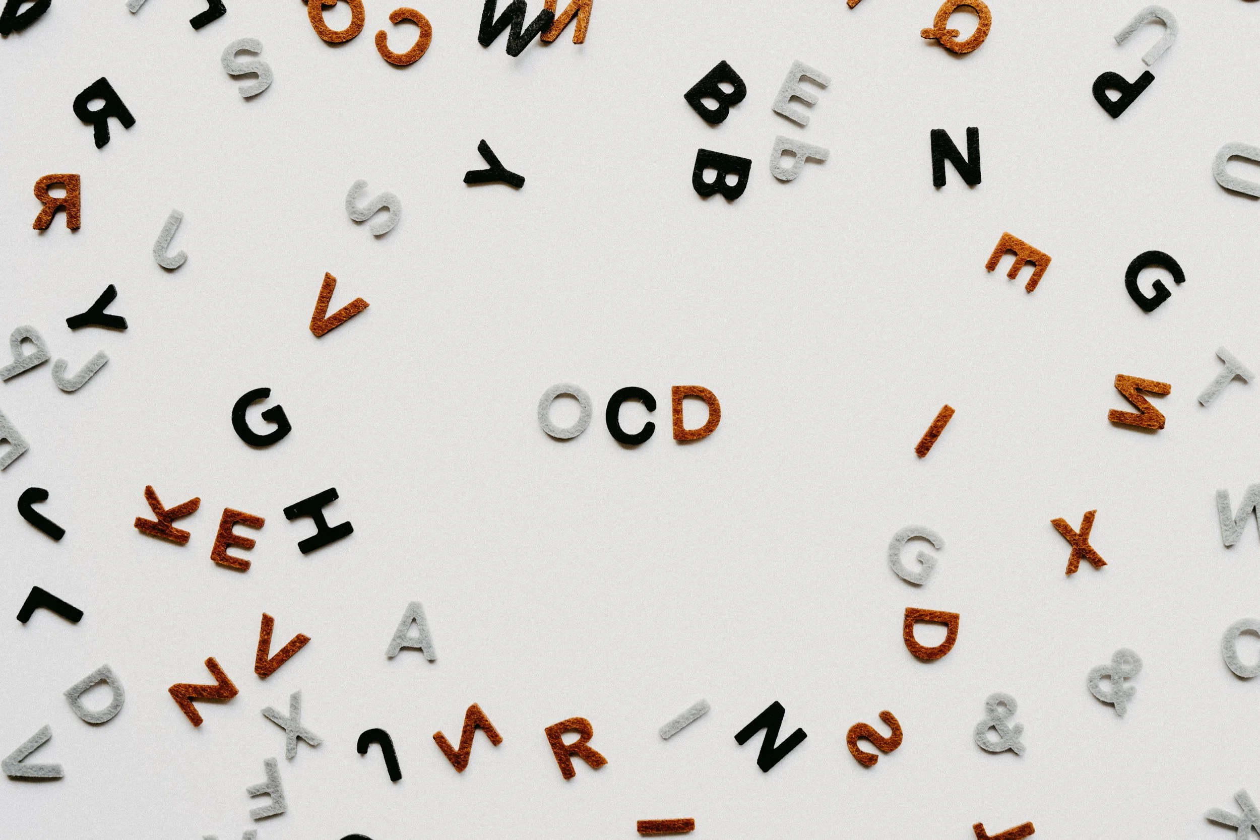 Colorful alphabet letter beads scattered on a white surface, spelling out 'OCD' in the center.