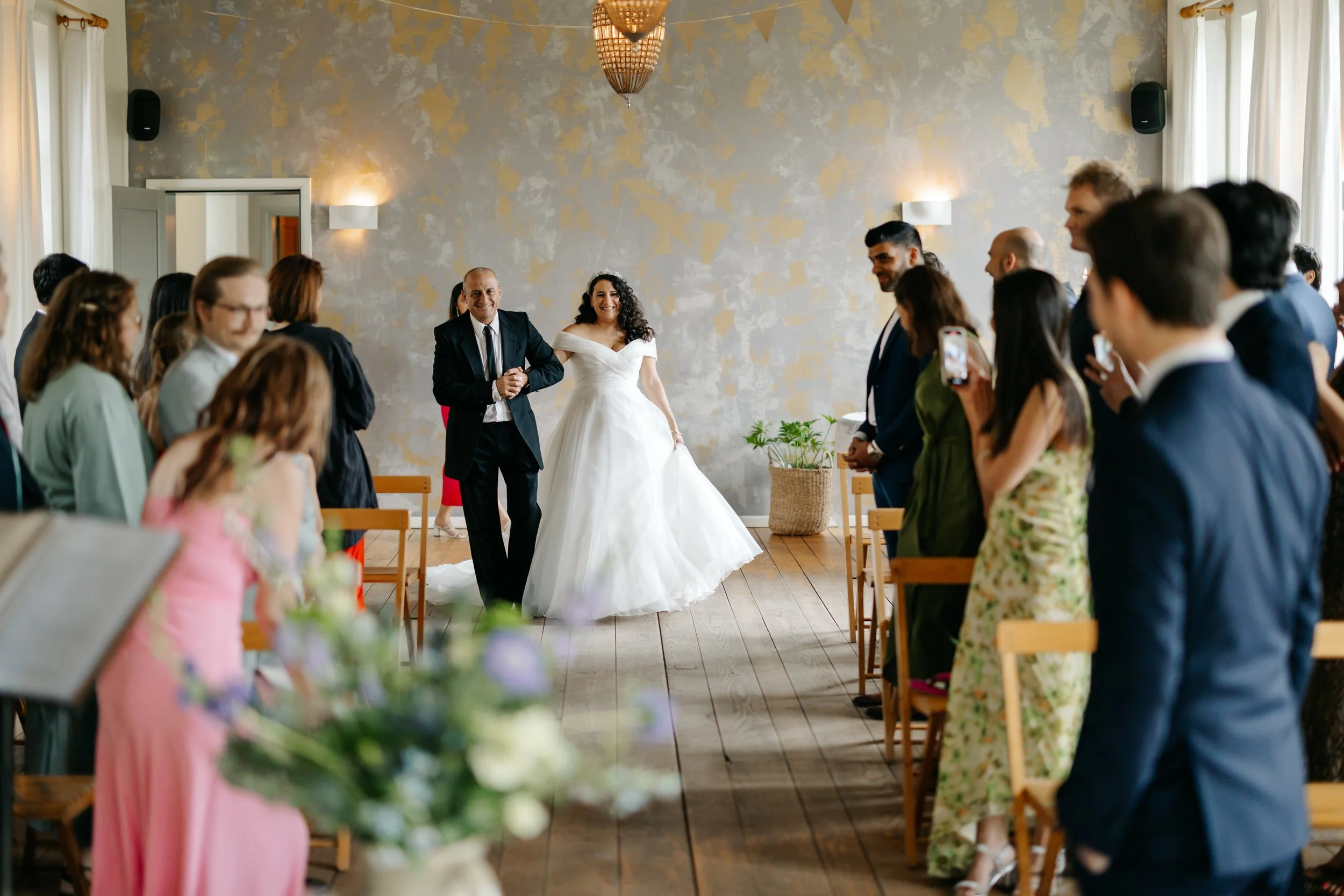 Yasmin loopt samen met haar vader het gangpad in tijdens de ceremonie bij Kasteel Tongelaar in Mill, met gasten aan beide kanten.