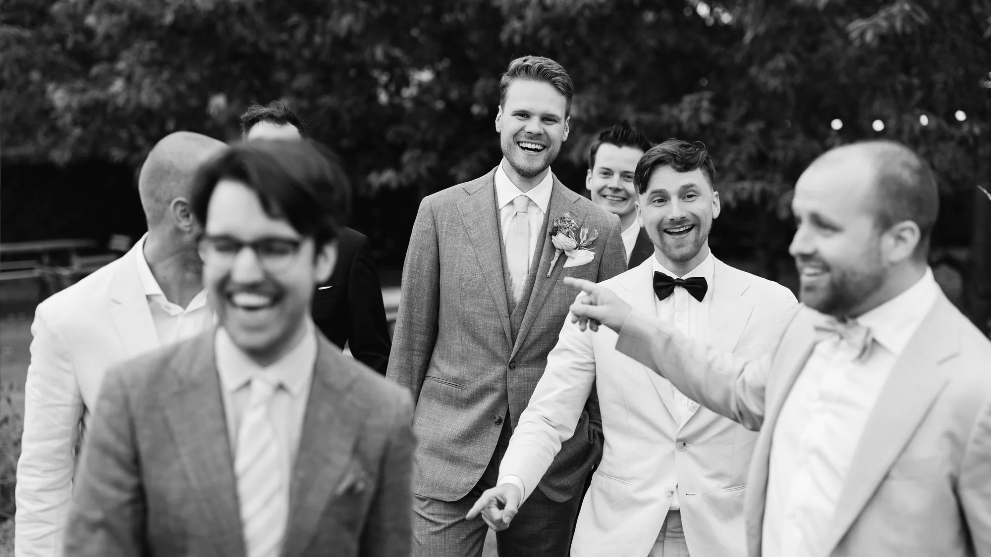  Bruidegom lacht met vrienden in de boomgaard tijdens de receptie 