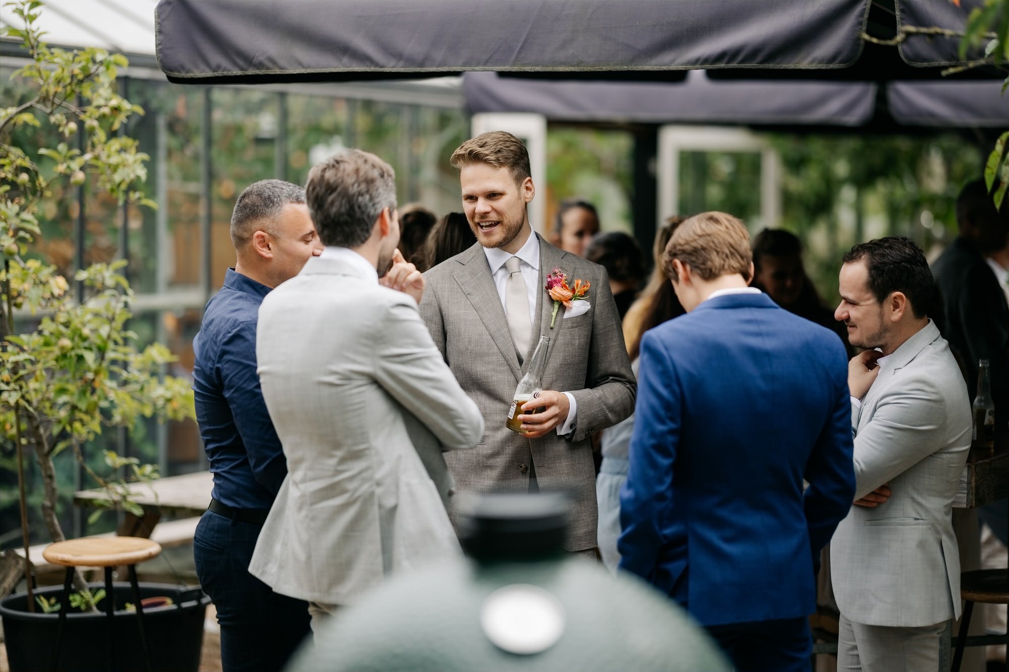  Bruidegom praat gezellig met gasten tijdens de receptie in de boomgaard 