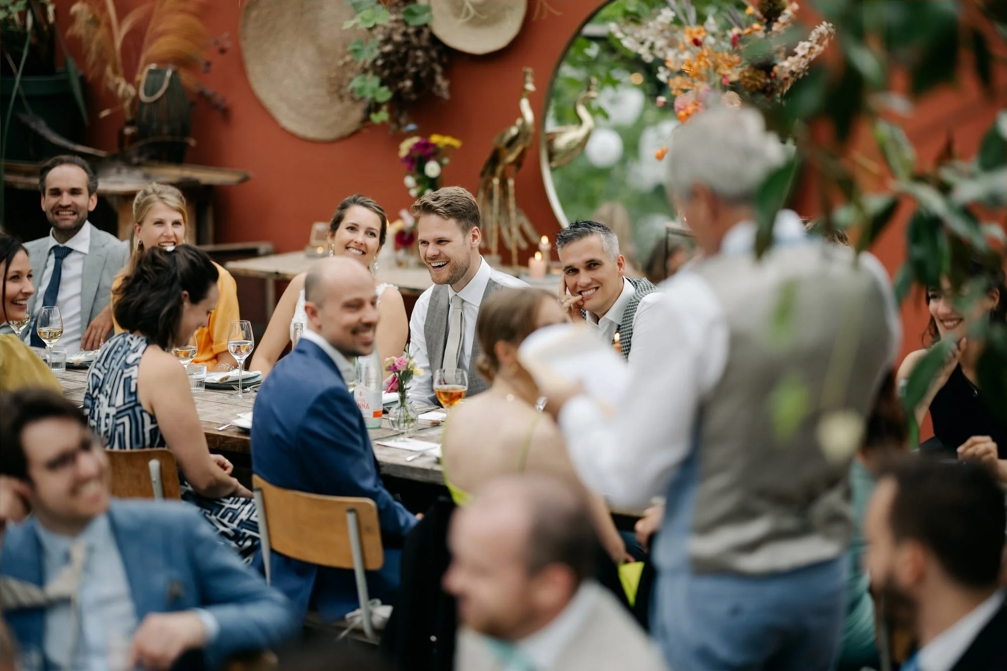  Bruidspaar luistert lachend naar een speech tijdens het diner in de kas 