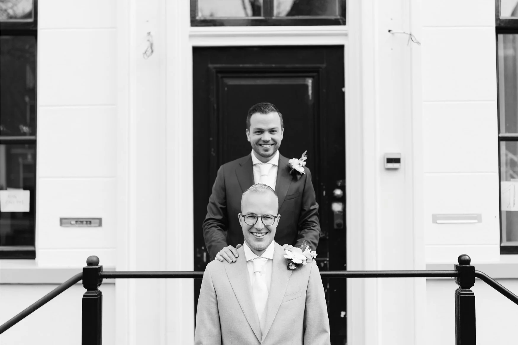  Zwart-witfoto van bruidegom die zijn partner van achteren omhelst bij een karakteristieke voordeur in Delft 