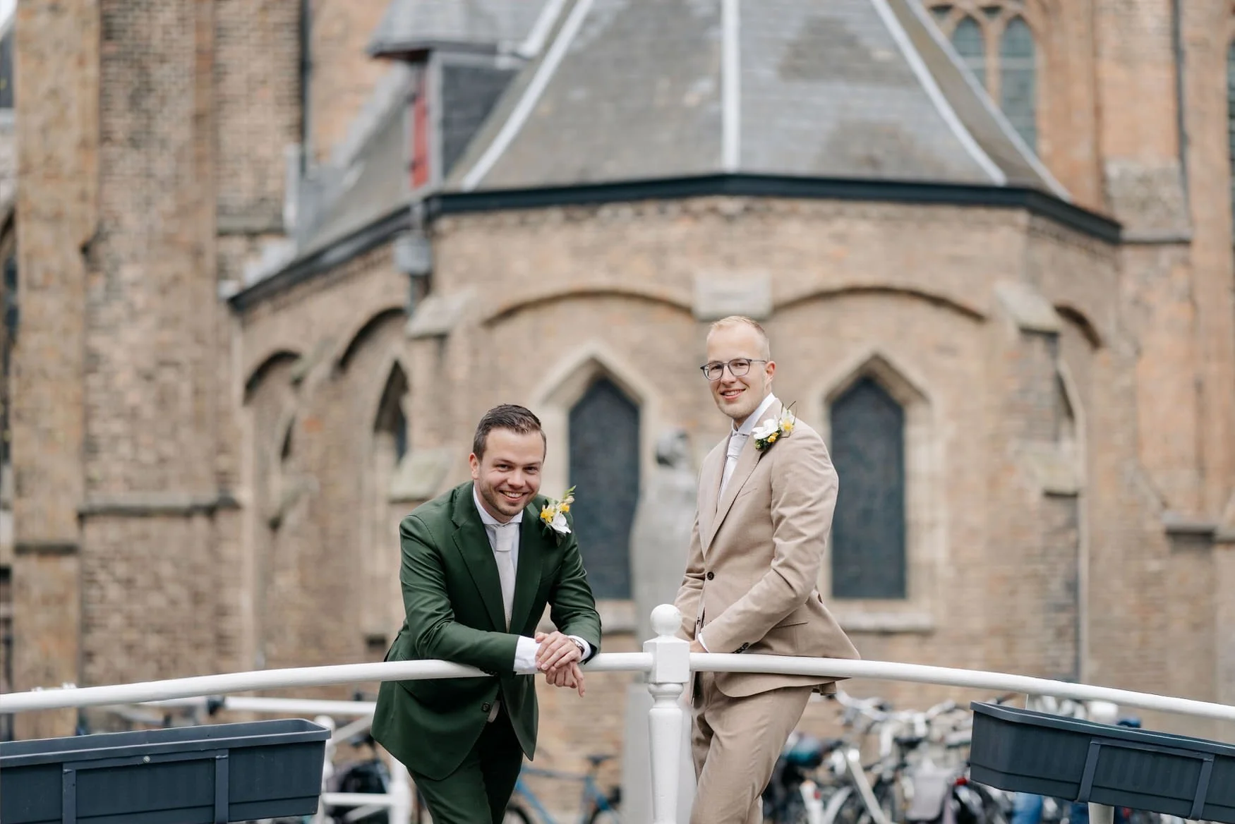  Bruidegoms leunen lachend over een brugleuning bij een kerktoren in Delft 