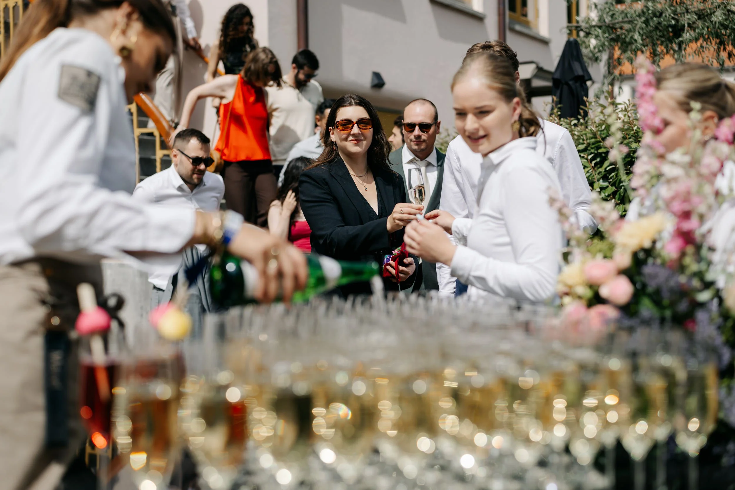  Medewerkers schenken champagne in voor de gasten tijdens de borrel buiten tussen de bloemen. 