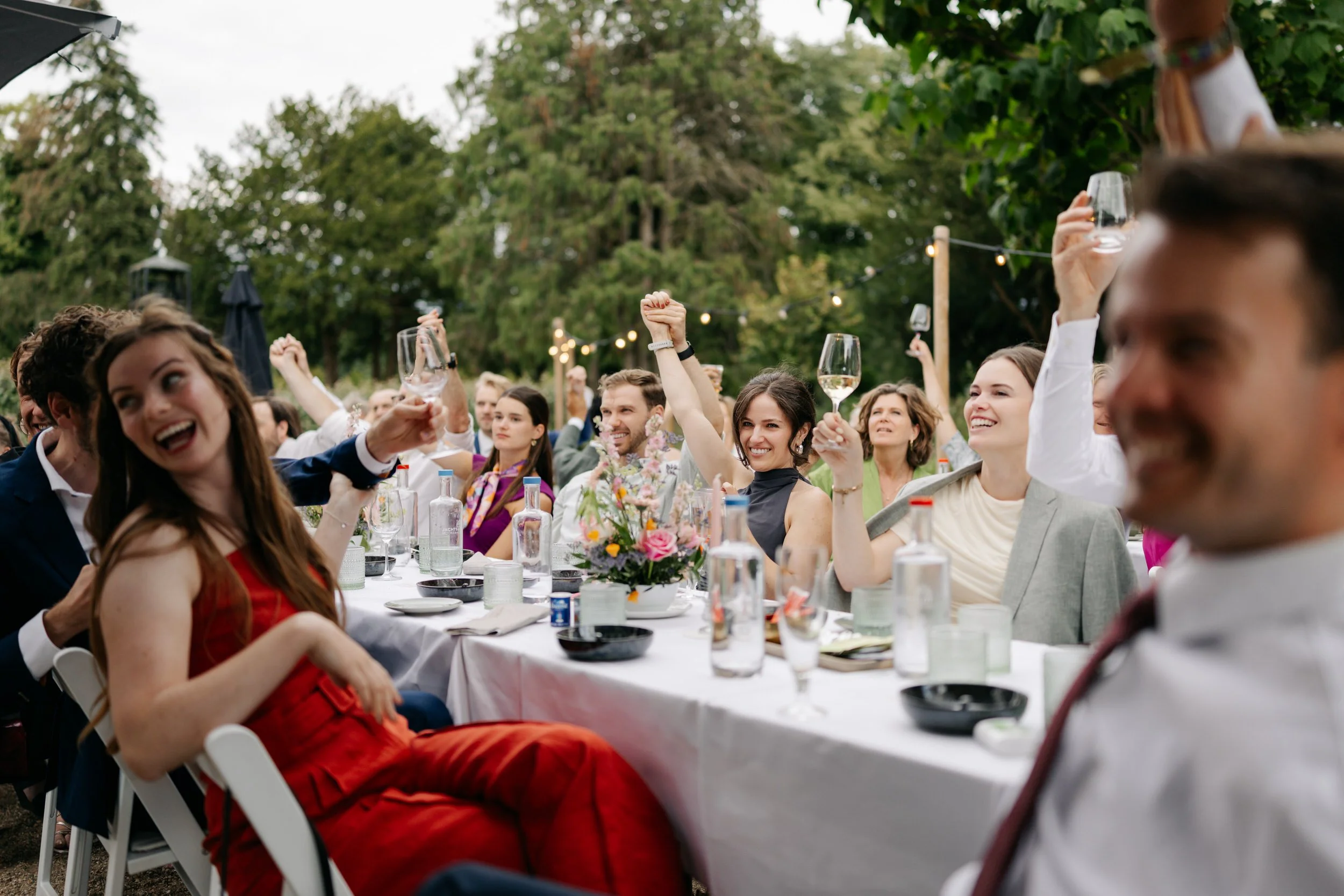  Gasten juichen en heffen hun glas tijdens een speech aan de feesttafel, avondsfeer op het terras. 