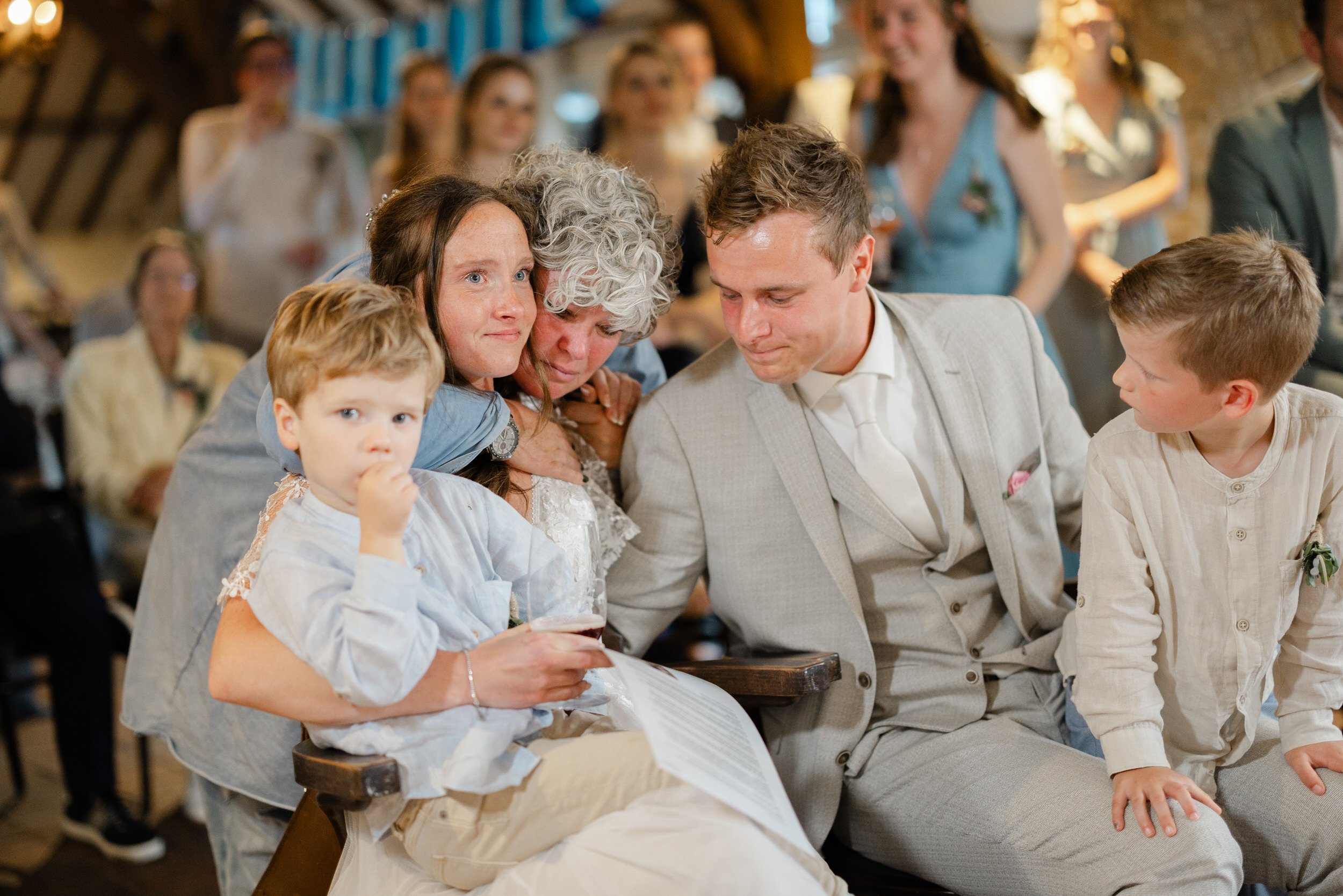 Bruidspaar met kinderen tijdens een warm familiemoment op de bruiloft, spontane foto vol verbinding