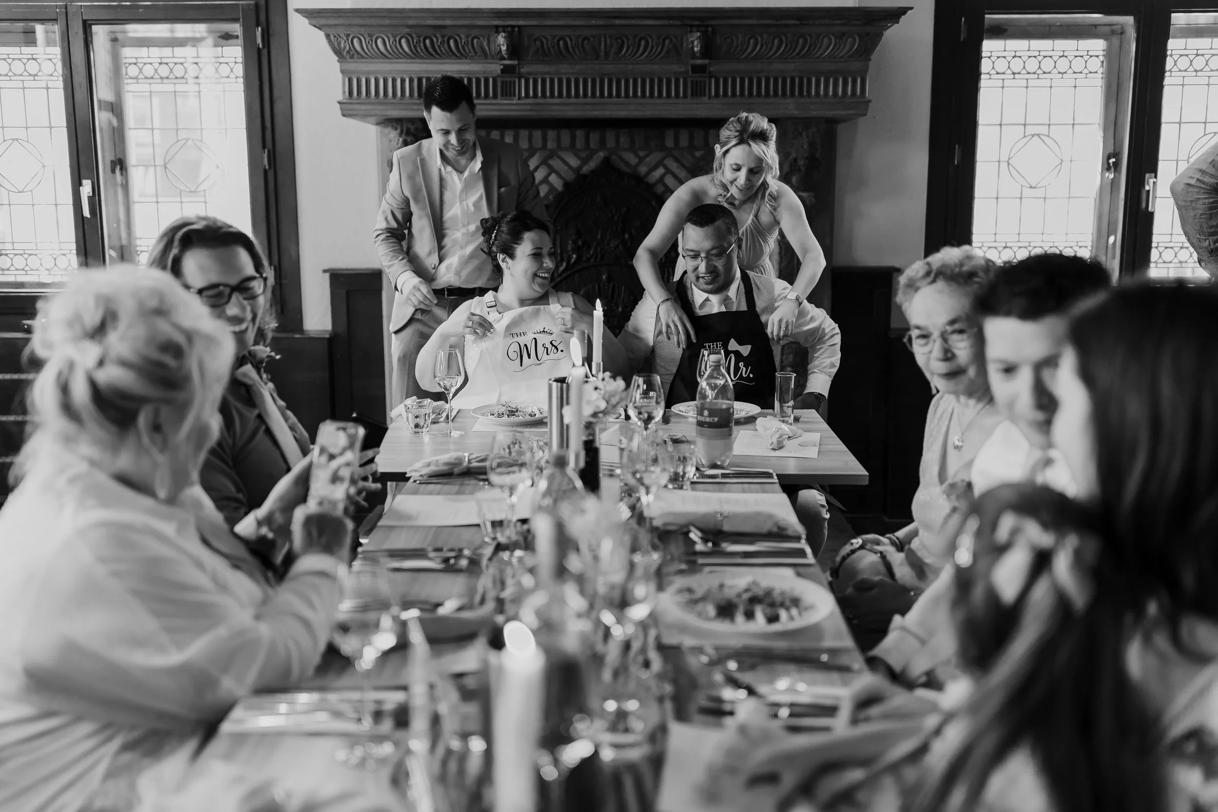 Gasten zitten samen aan tafel tijdens een diner op de bruiloft, zwart wit reportagebeeld vol sfeer en verbinding