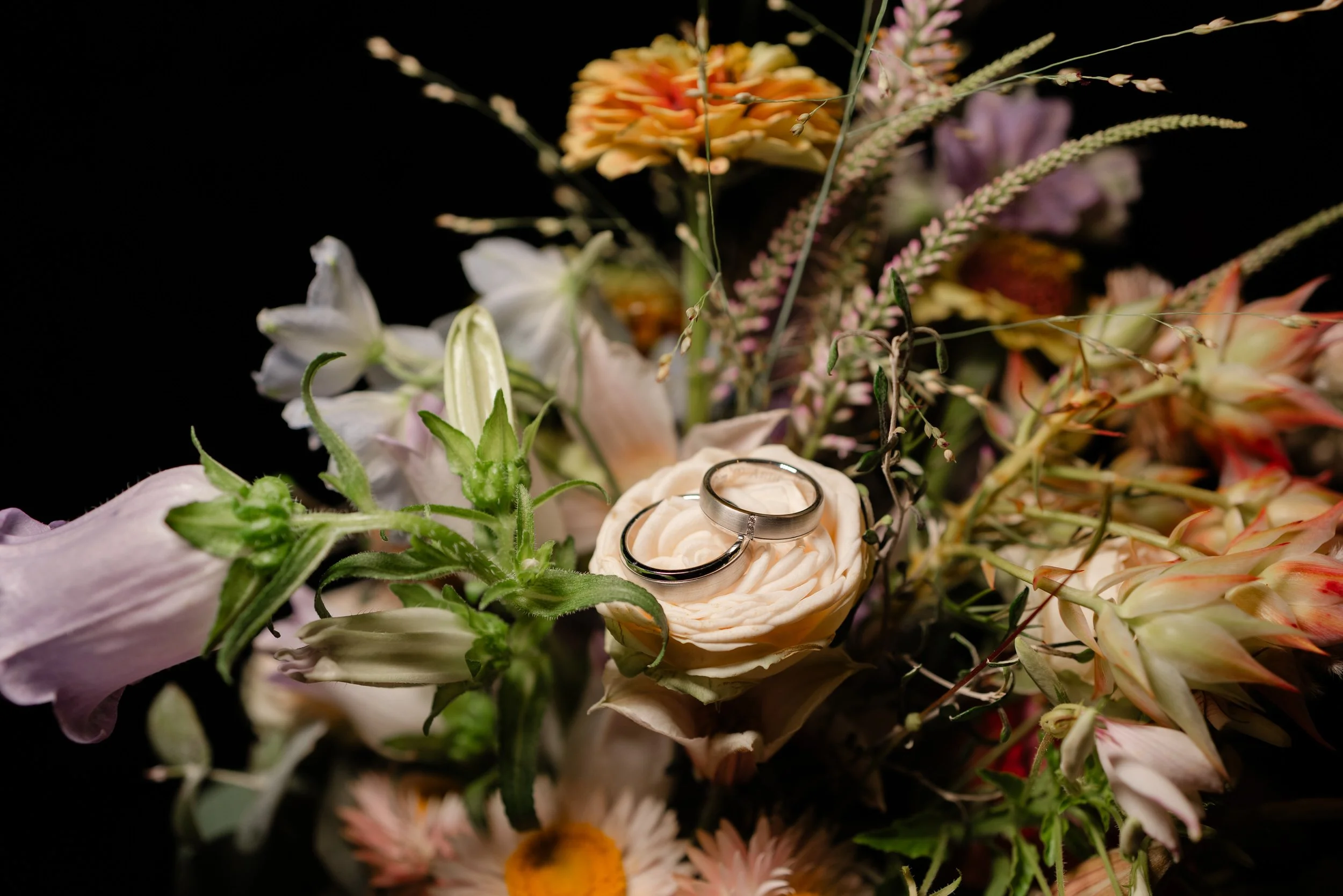 Trouwringen liggen op een bloemstuk, detailfoto van sieraden en styling op de trouwdag