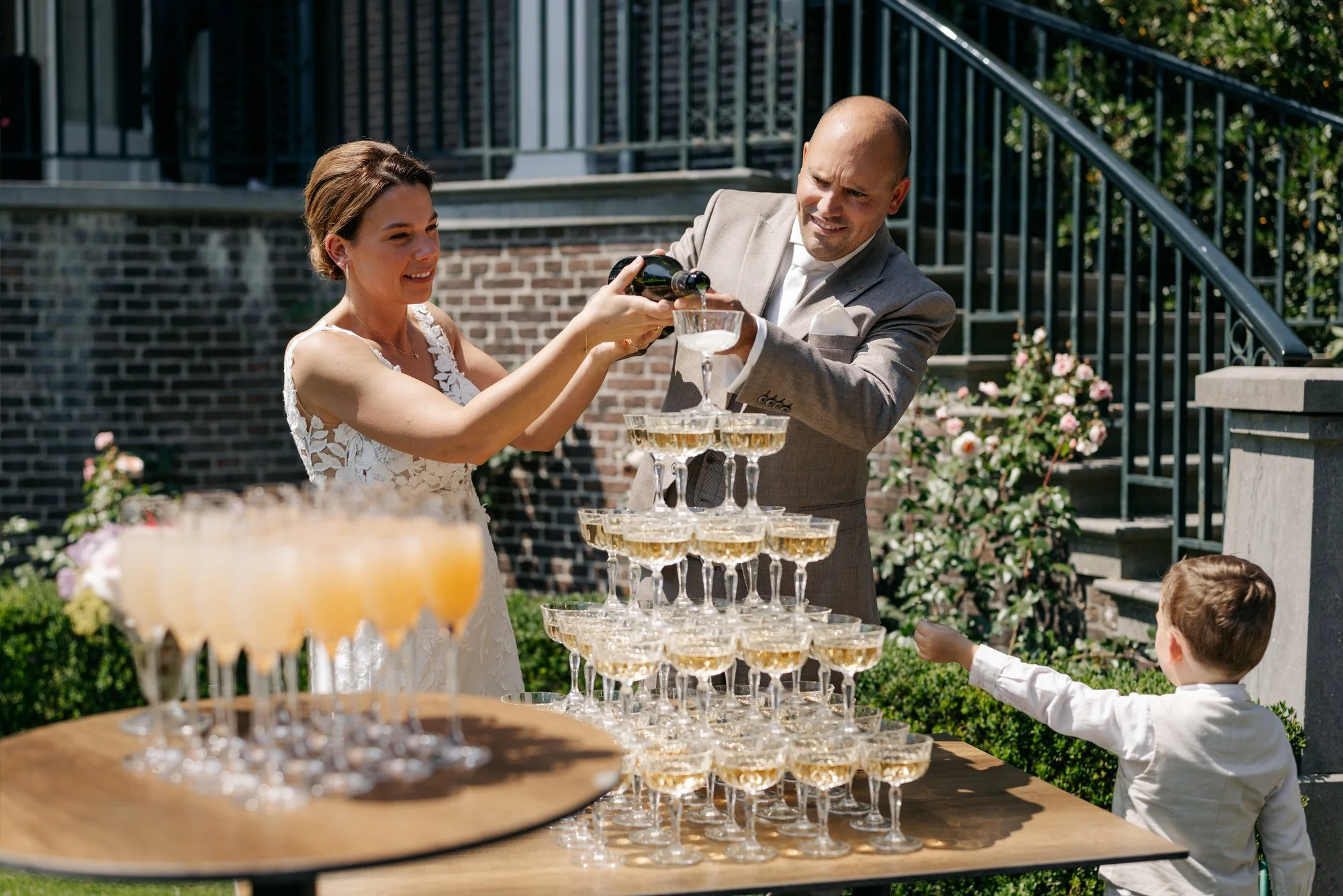 bruidspaar schenkt champagnetoren tijdens zonnige bruiloft
